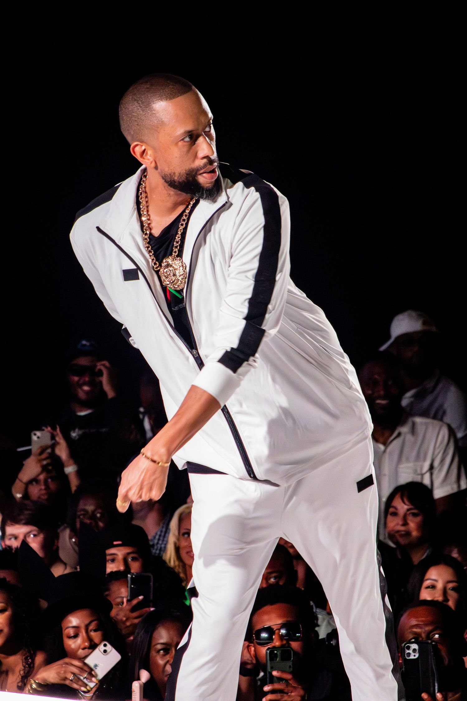 Performer in white tracksuit with black trim dances energetically on stage during nighttime performance.