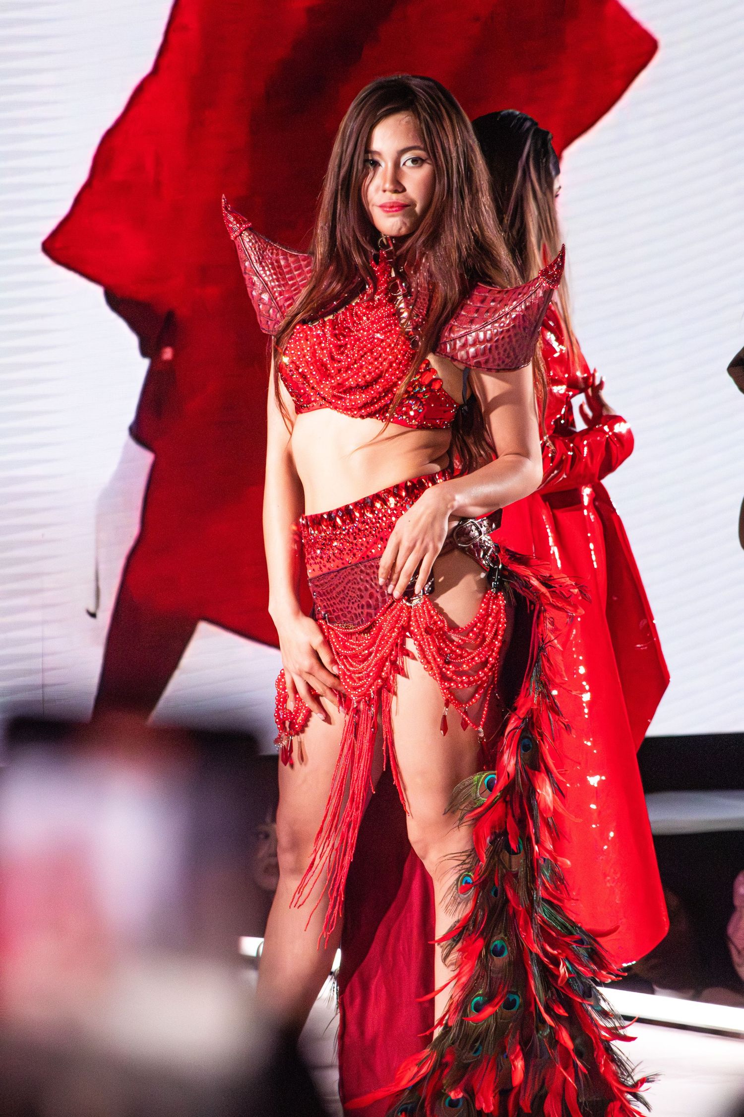 Model showcases intricate red beaded costume with dramatic cape on runway.