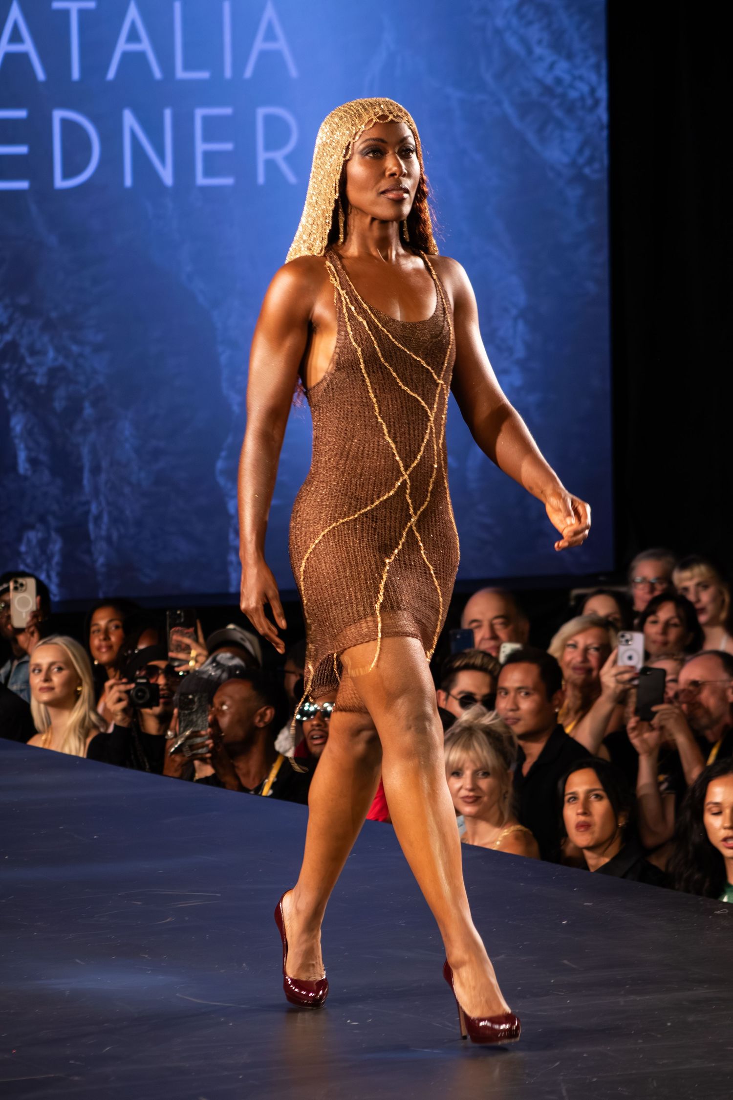 Model walks Natalia Fedner runway in brown knit chain-embellished mini dress with blonde braids.