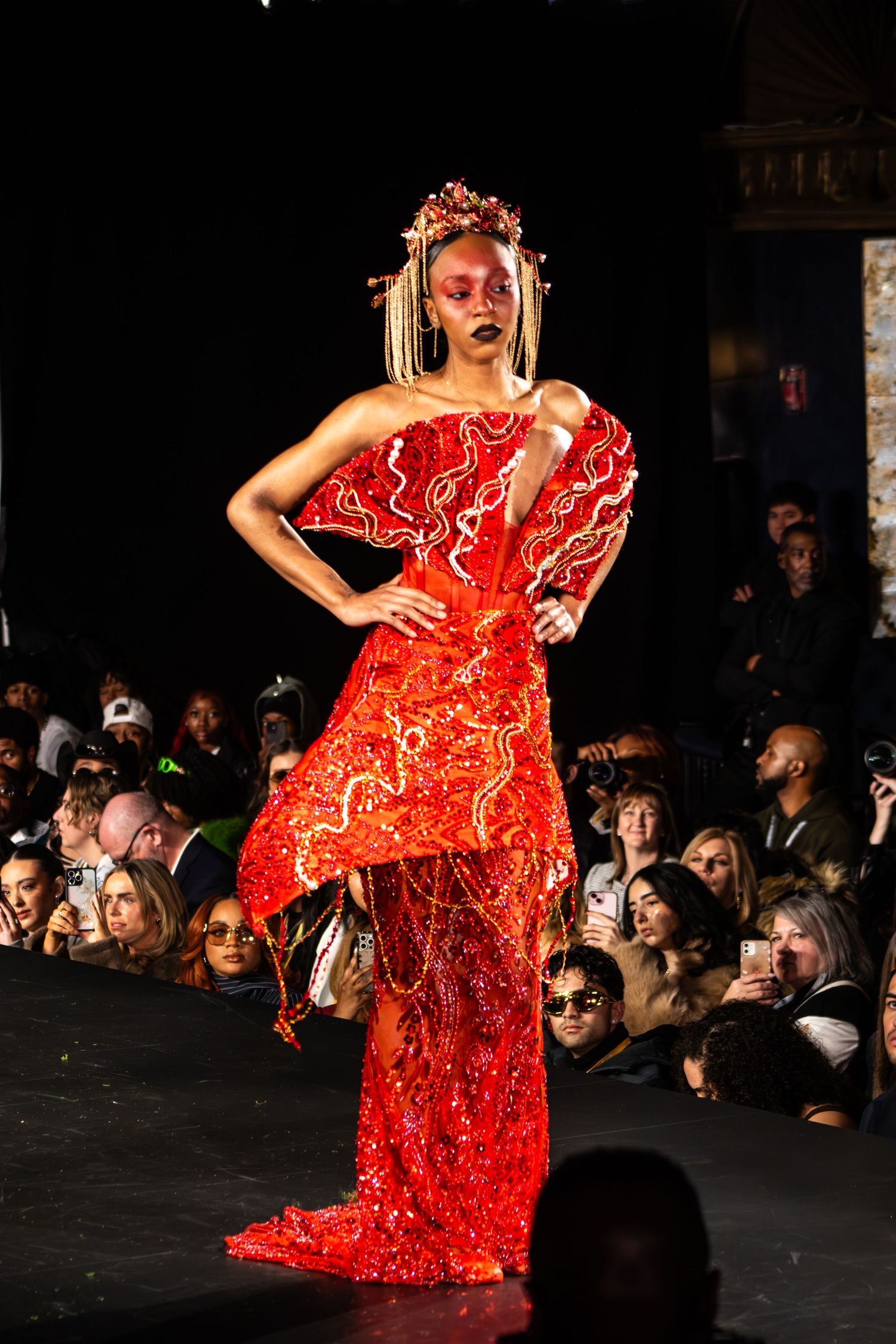 Model walks the runway in a dramatic red and white patterned one-shoulder evening gown during a fashion show.