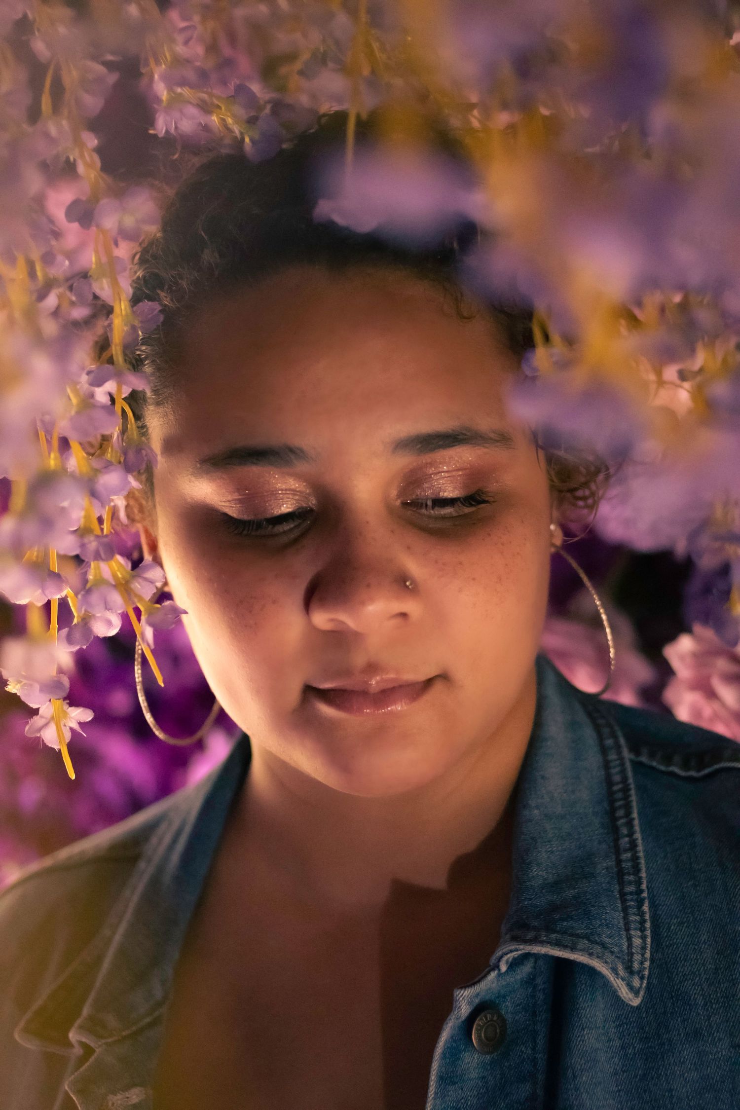 Artistic portrait with soft focus against purple wisteria flowers in dreamy lighting.