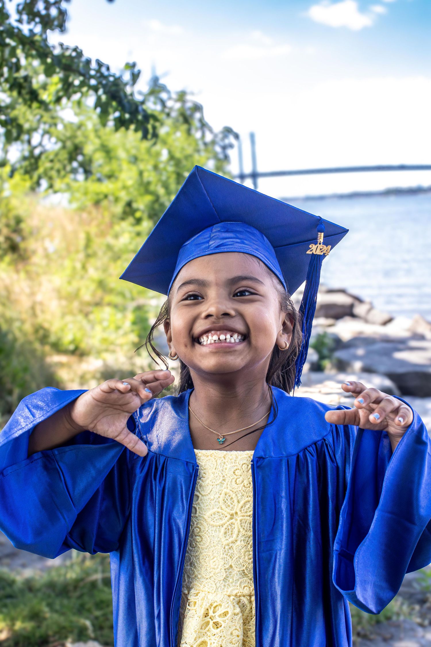 Graduate in blue cap and gown poses joyfully by the water.