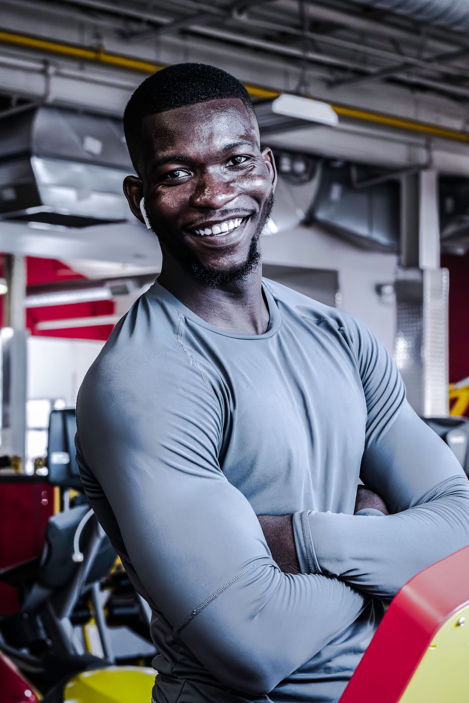 Athletic person in grey workout shirt smiling confidently in gym setting.