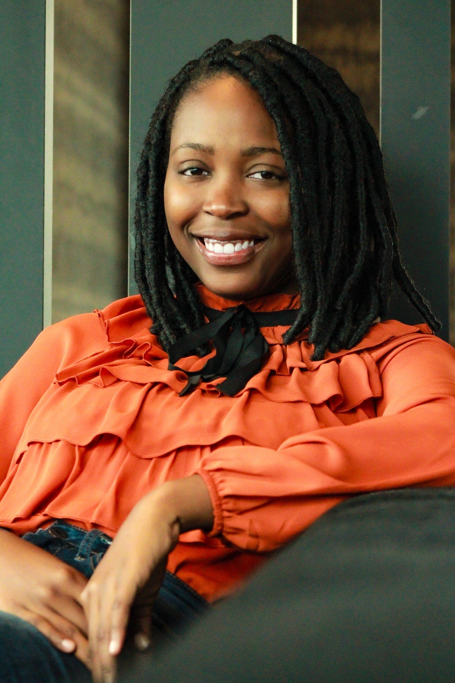 Stylish portrait featuring a ruffled coral blouse and natural locs hairstyle against a modern backdrop.
