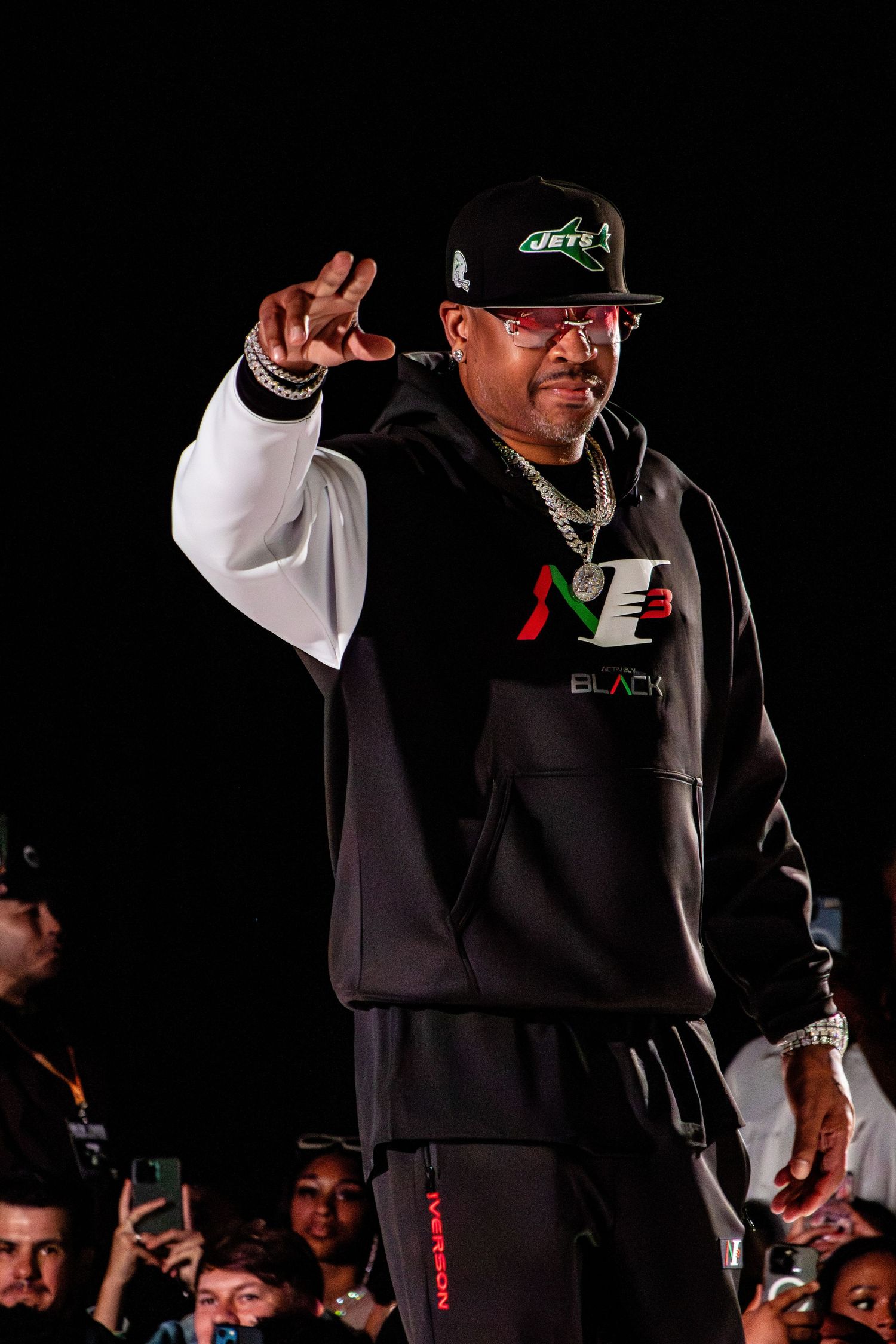 Performer in black and white sports attire gestures to crowd while wearing NY Jets cap.