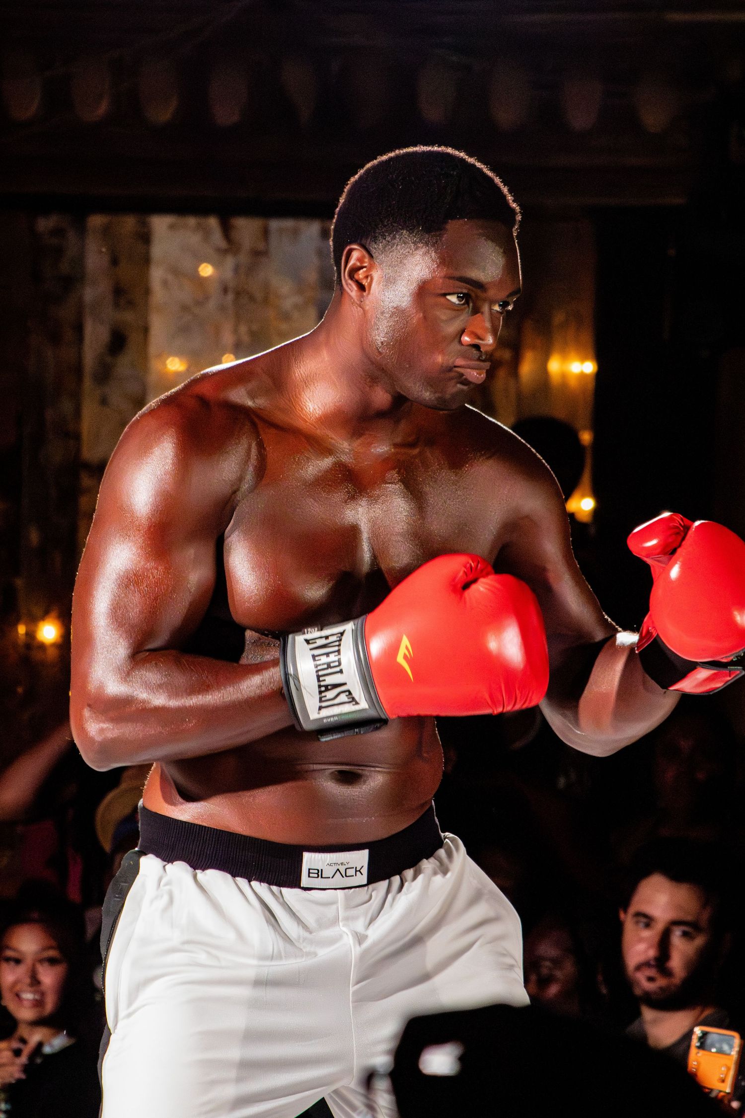 Boxer in white shorts and red gloves poses in fighting stance during performance.