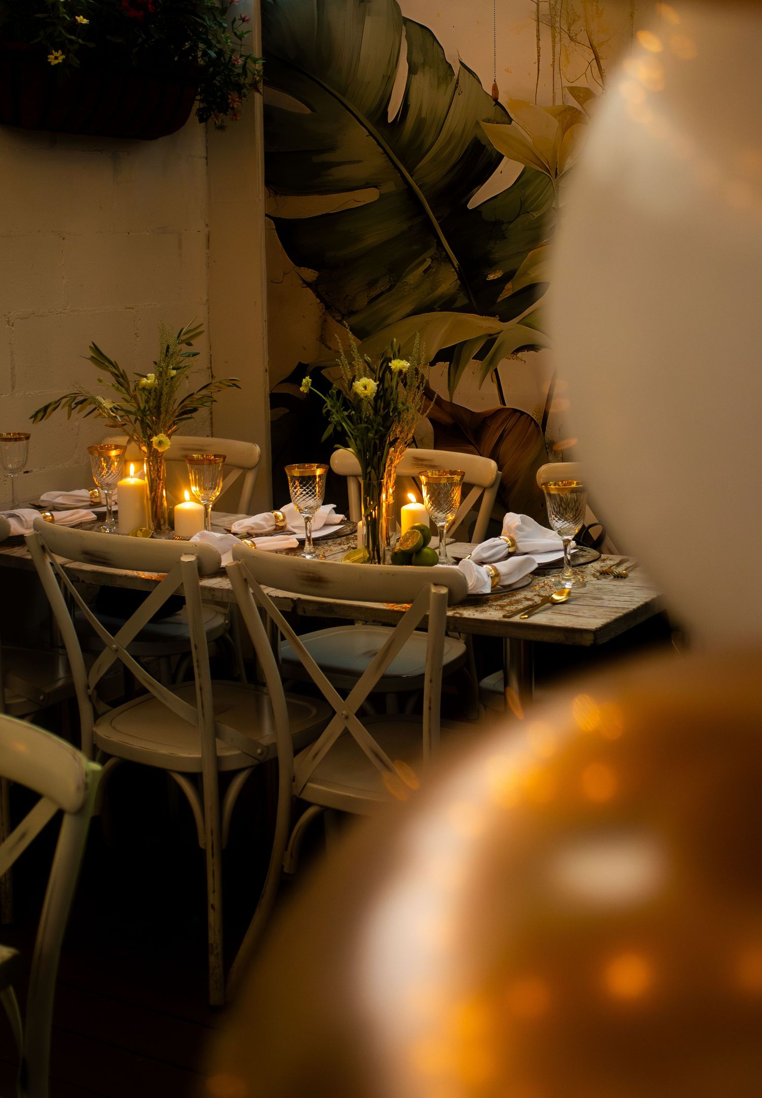 Elegant candlelit dining table with tropical leaf decor, floral centerpieces, and gold accents for an intimate event.