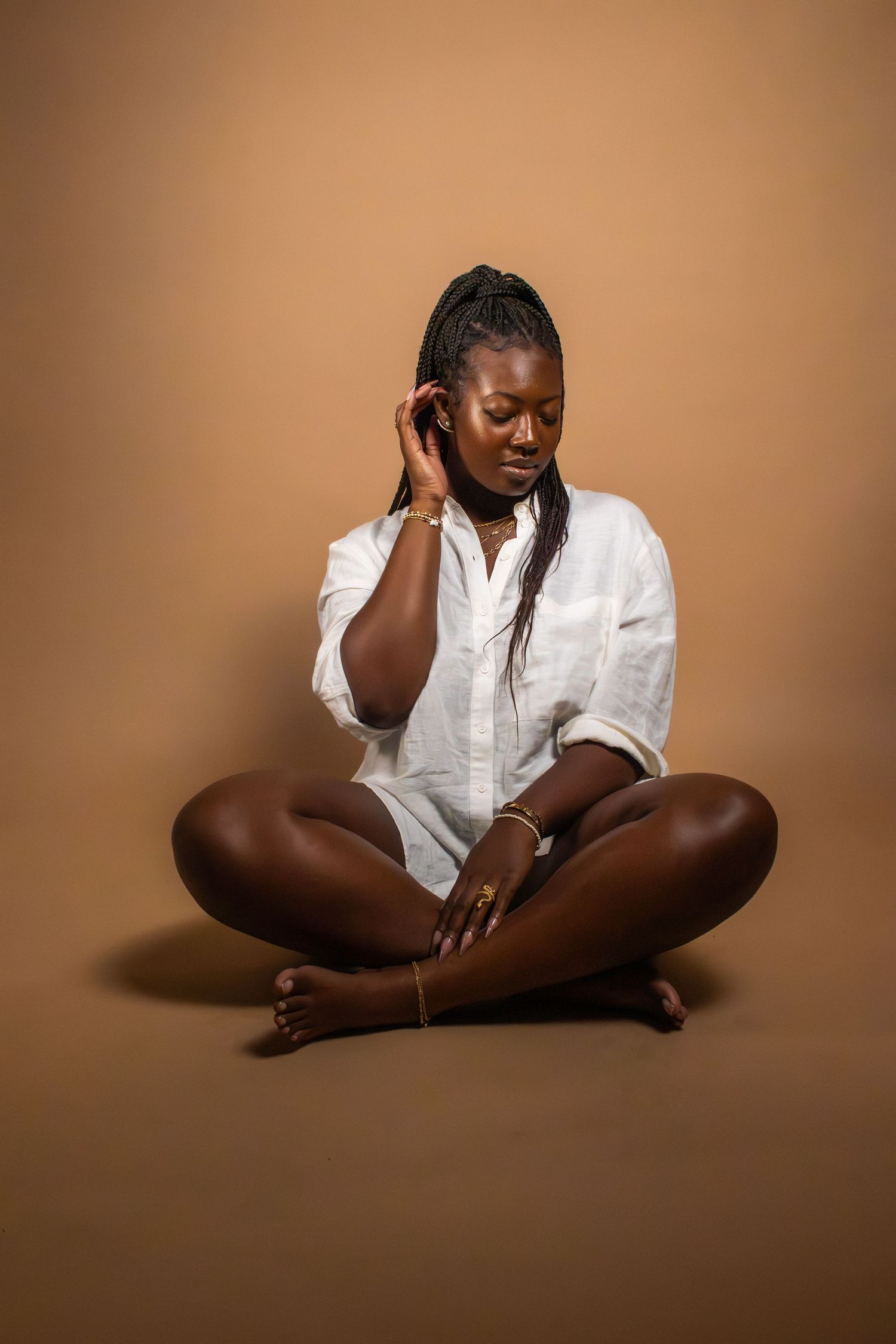 Person in white shirt sits cross-legged in contemplative pose against brown backdrop.