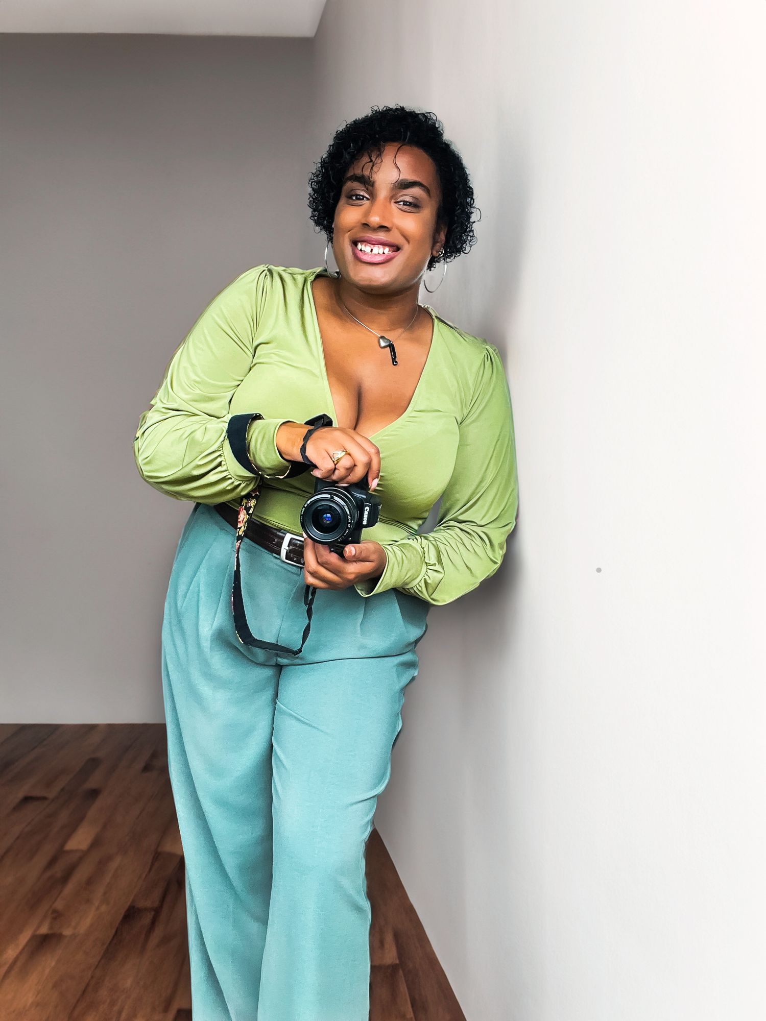 Joyful photographer holding camera in modern kitchen space wearing bright spring colors.