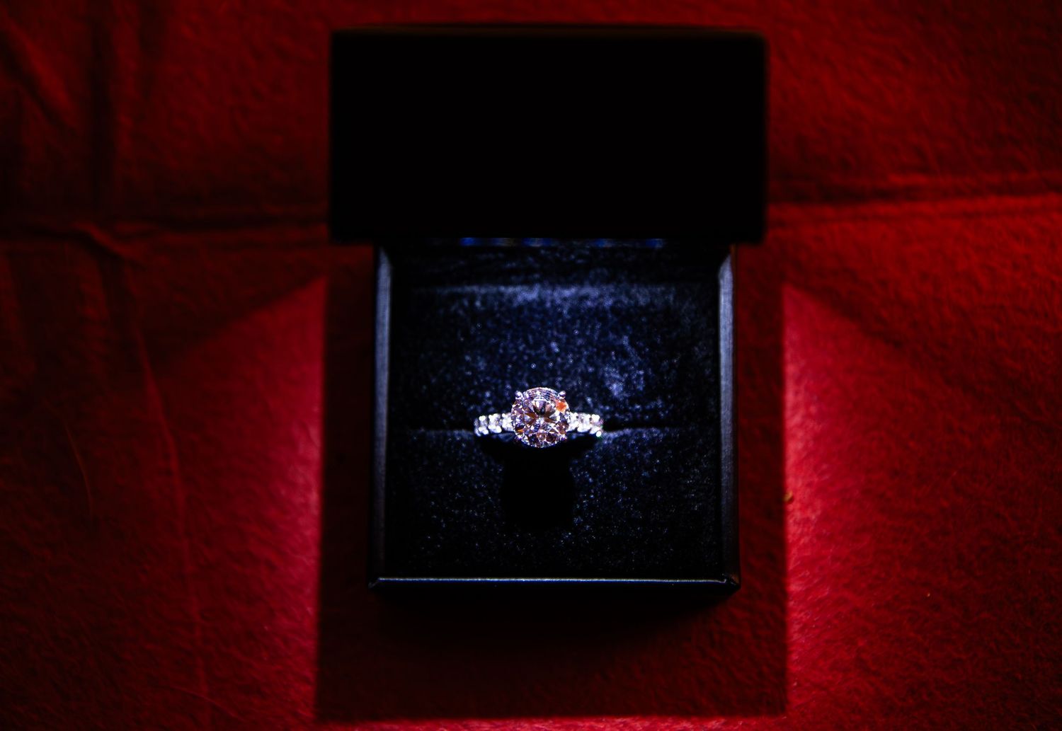 Silver ring with pink gemstone displayed in black jewelry box on red velvet background.