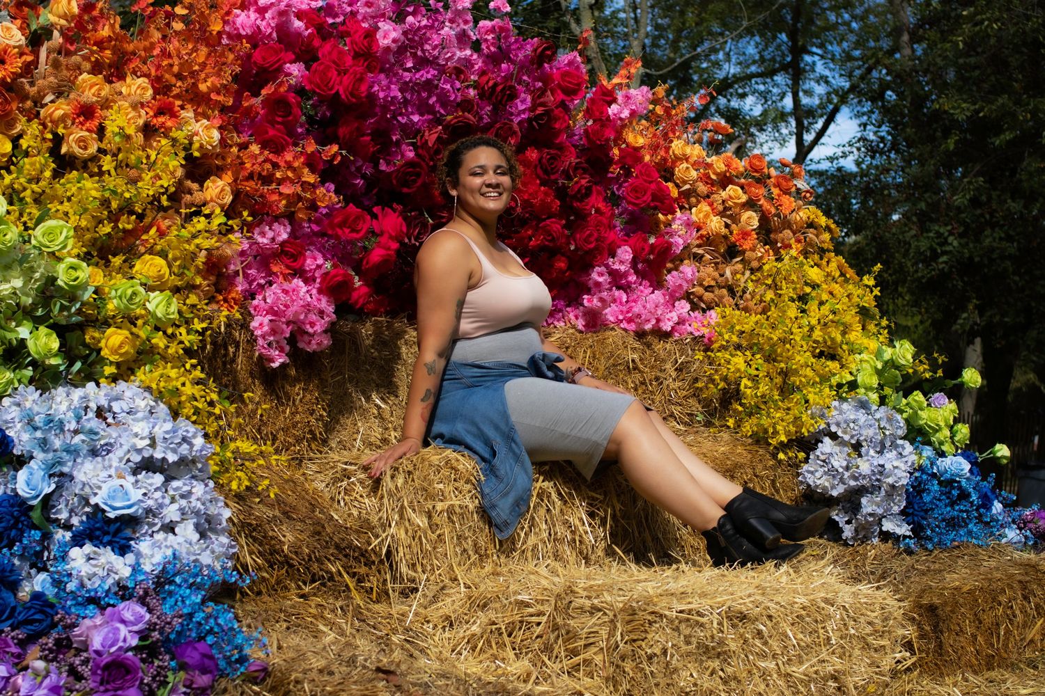 Colorful floral display with rainbow gradient flowers surrounding a hay bale in outdoor setting.