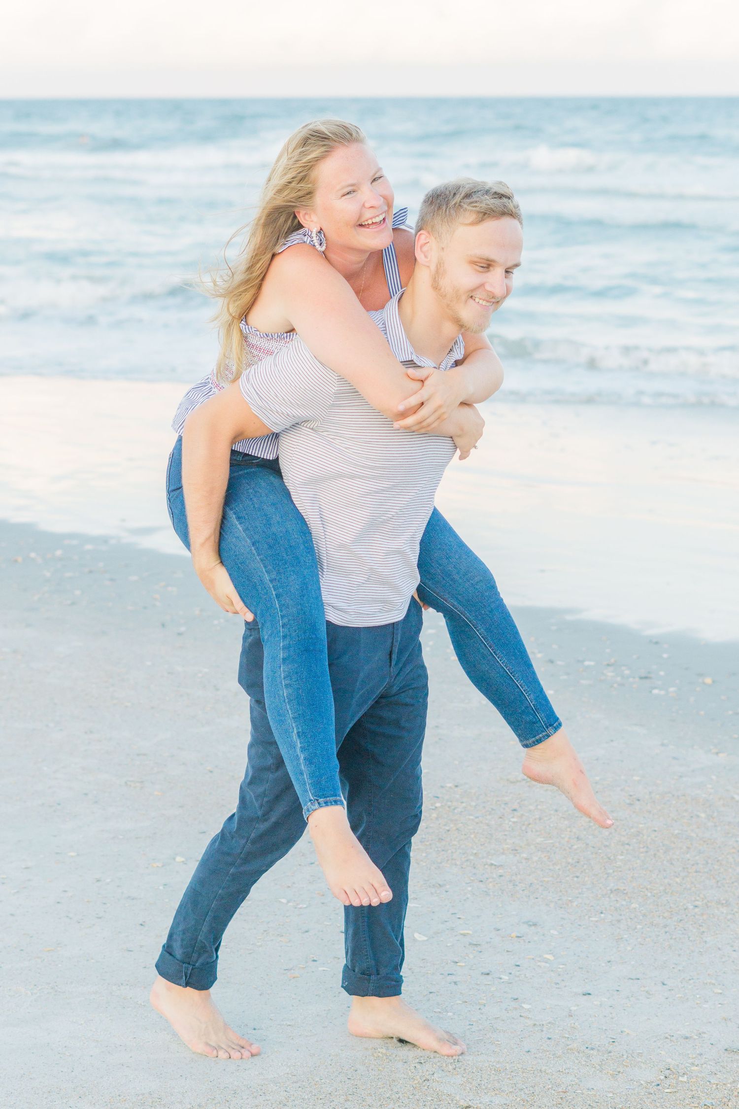 A couple plays and laughs during a piggyback ride along the beach.