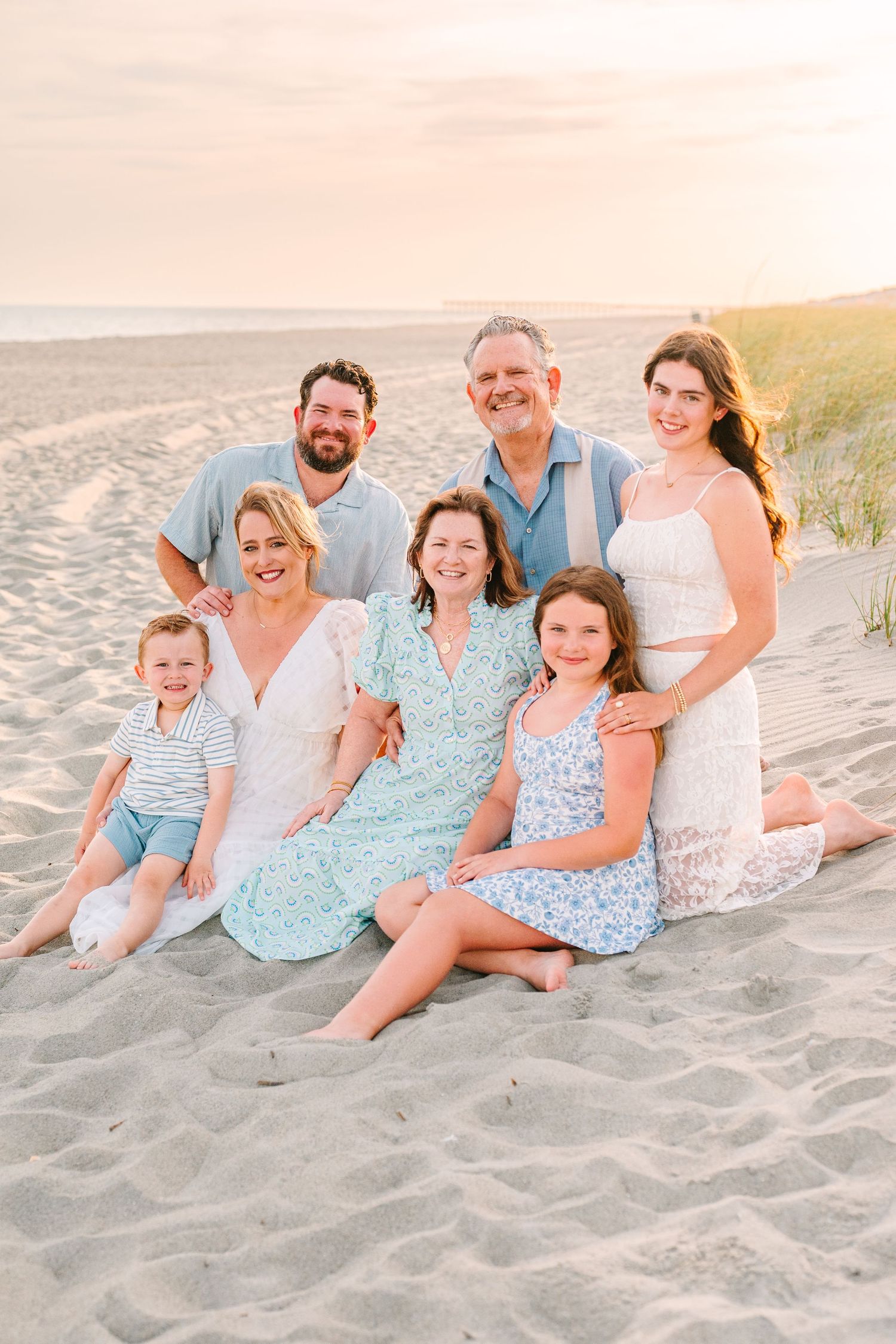 A group in coordinated blue and white outfits poses together on a sandy beach at sunset.