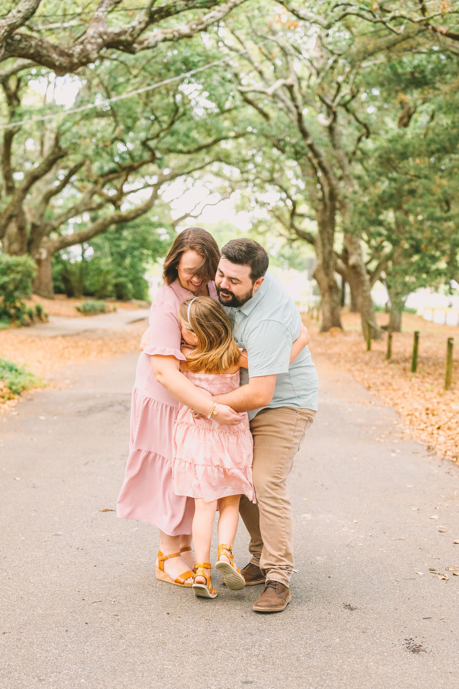 A family shares an intimate moment under a canopy of oak trees on a scenic path.