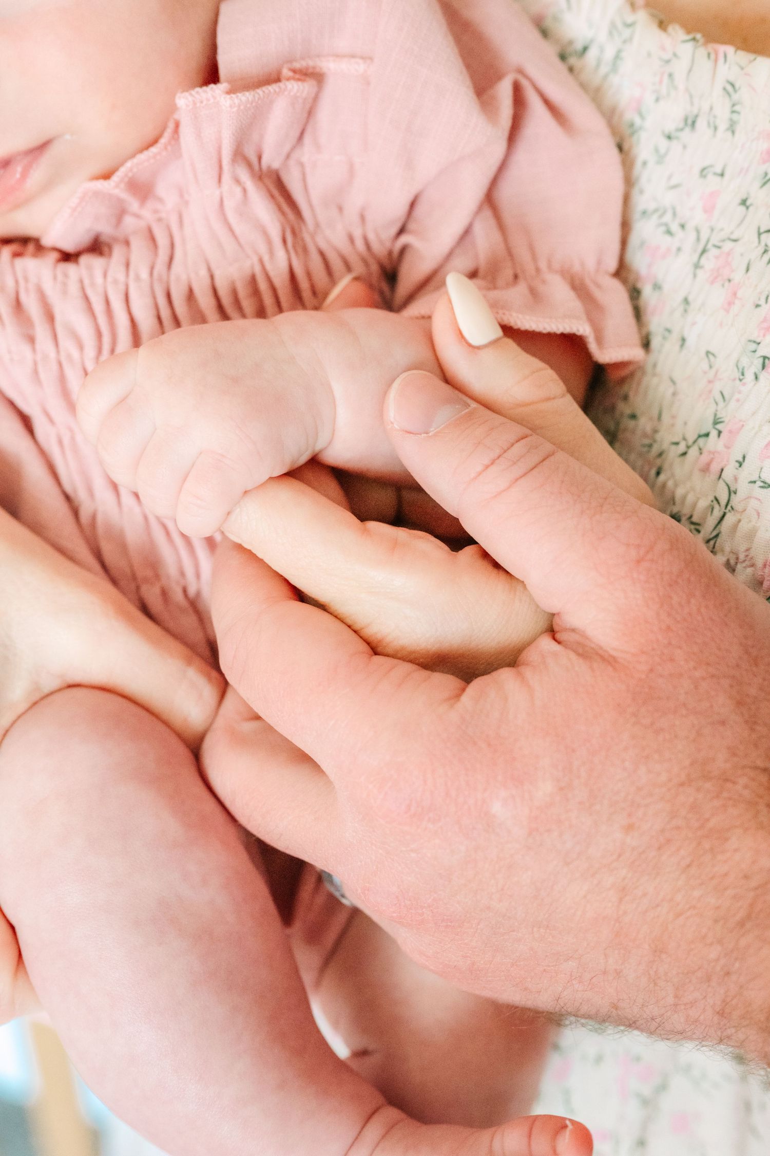 Close up of hands gently holding baby's feet wearing pink smocked romper.