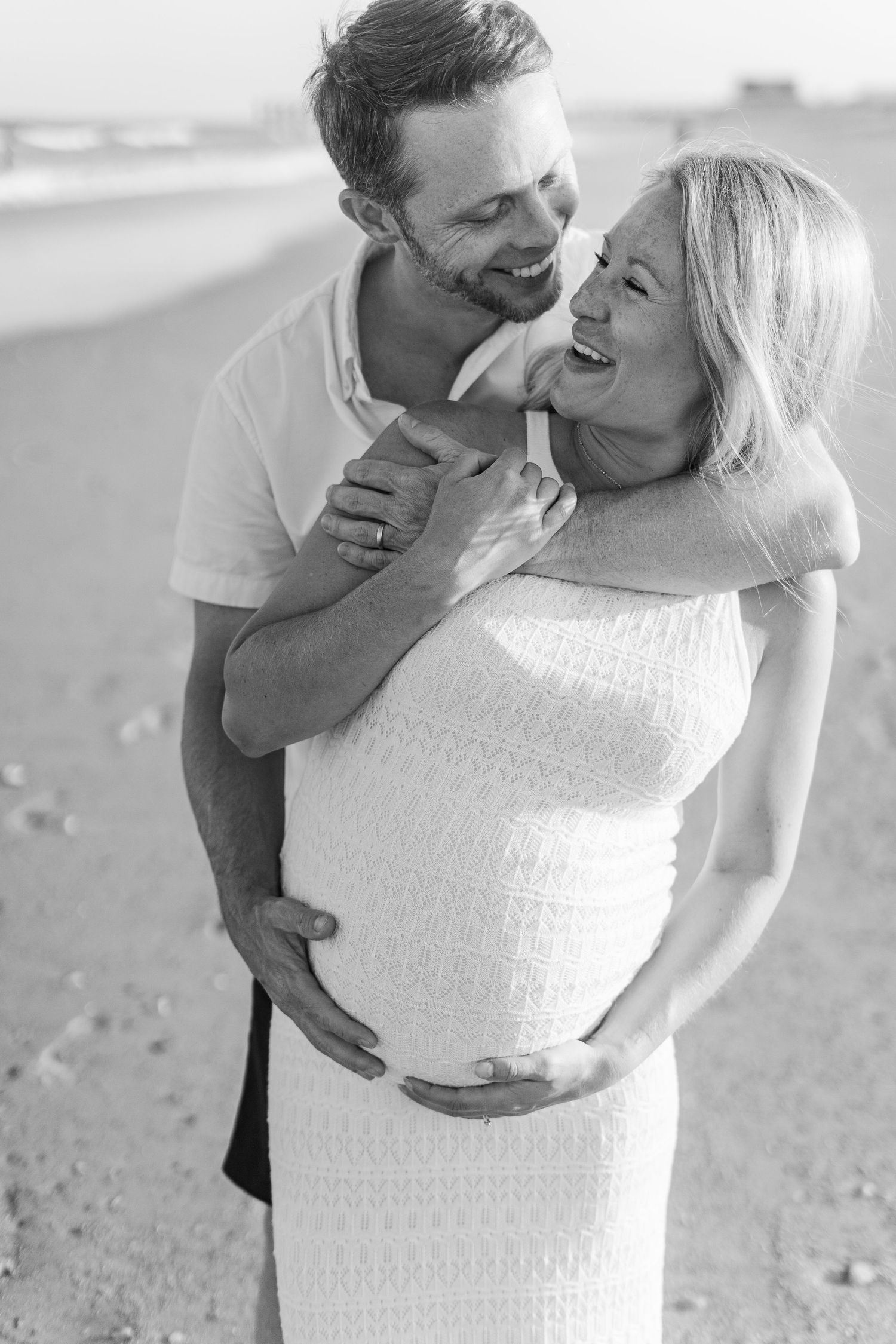 Candid moment between expecting couple during beach maternity photoshoot.