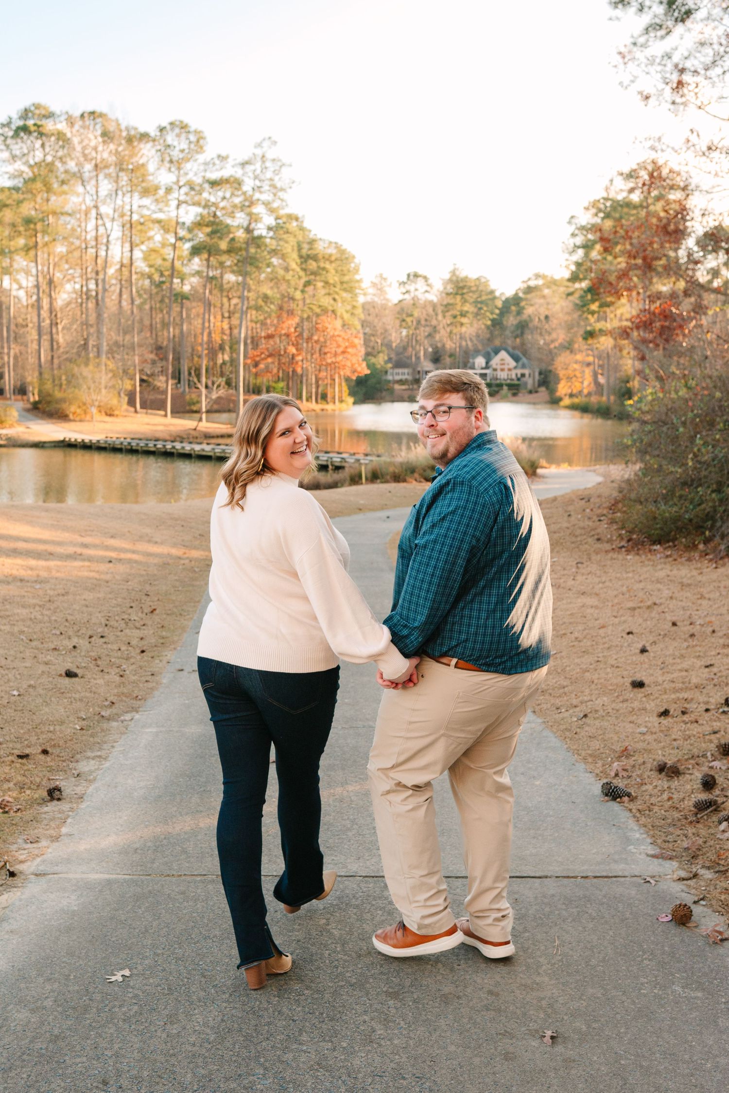 A couple holding hands while walking along a lakeside path during golden hour.