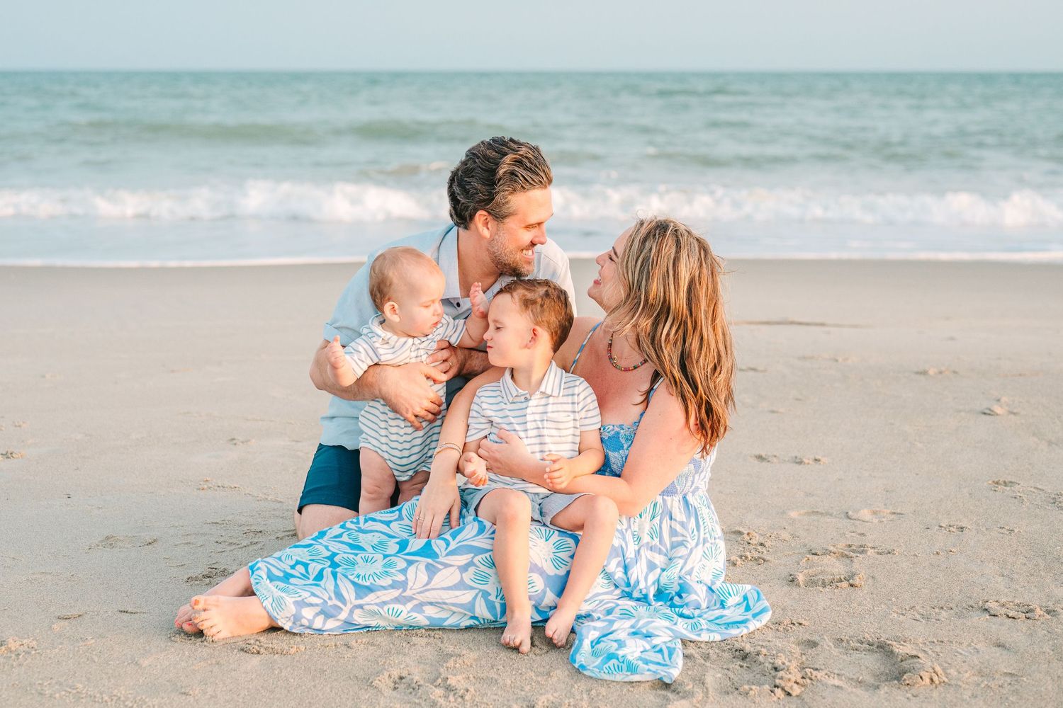 Family of four sitting close together on beach during golden hour.