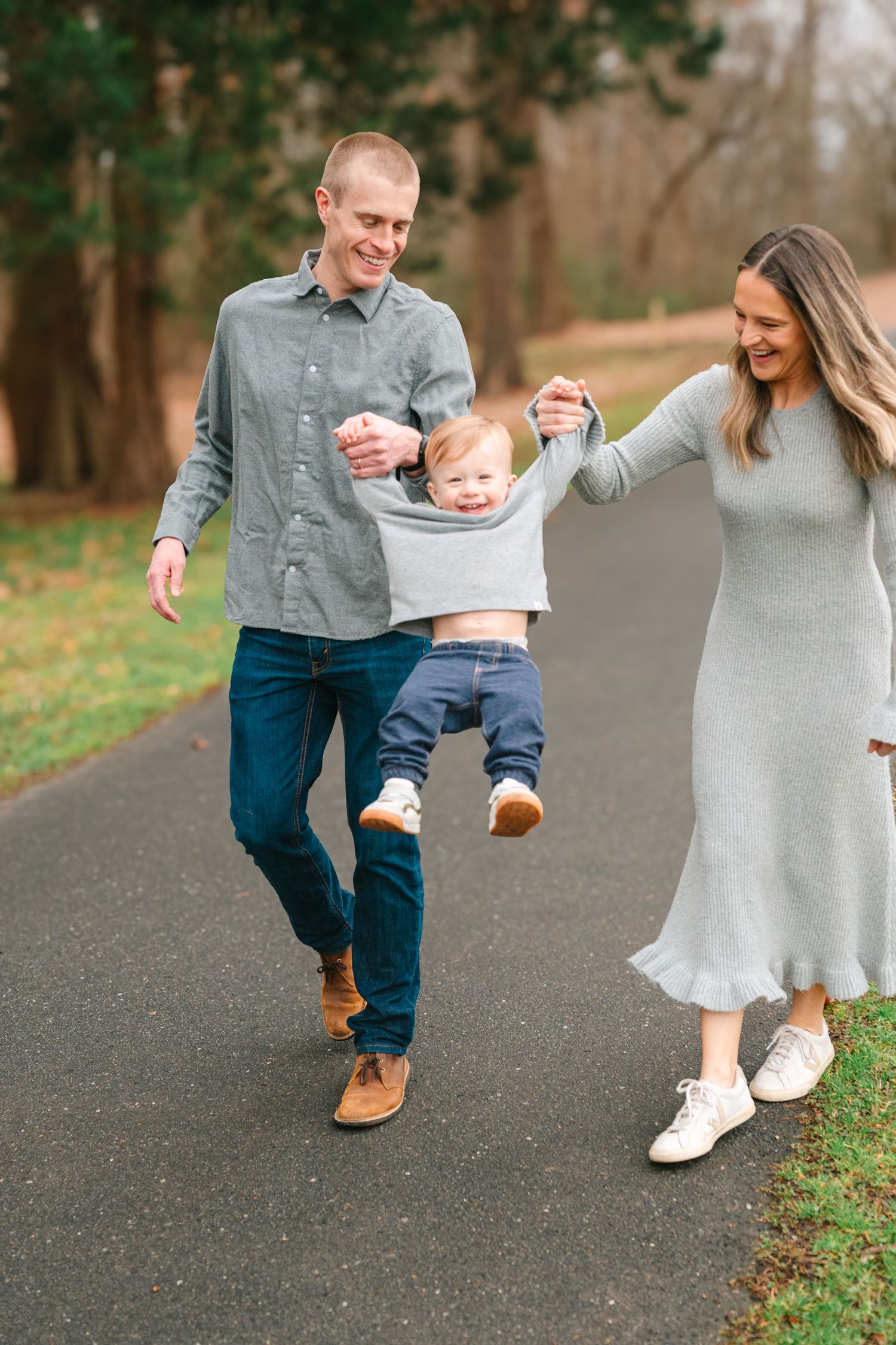 A family enjoys a playful moment together while walking on a path surrounded by trees.