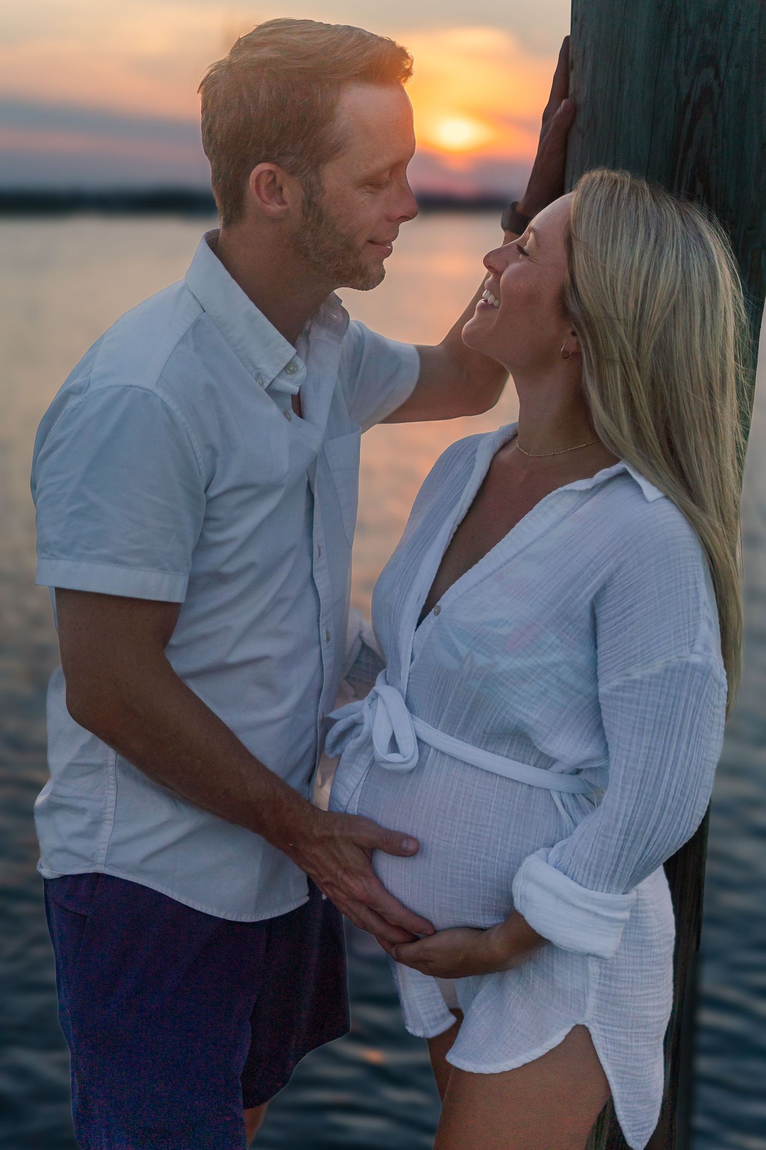 Tender moment between expecting couple during sunset beach photoshoot.