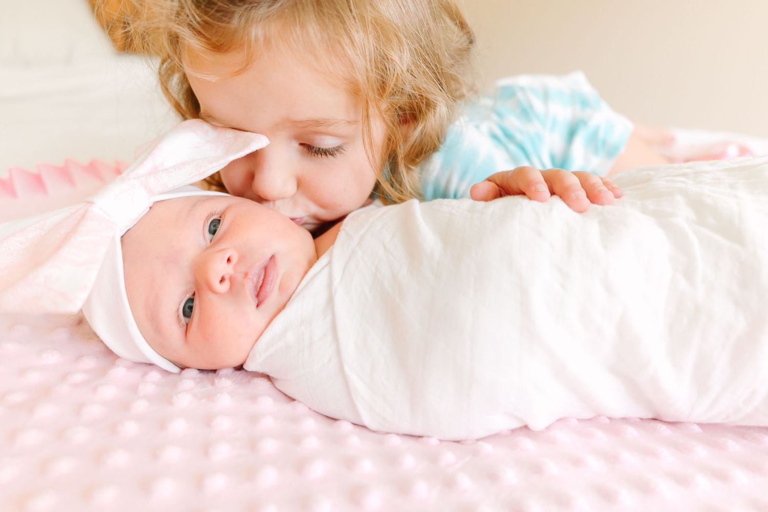 Two children share a tender moment on pink polka dot bedding.