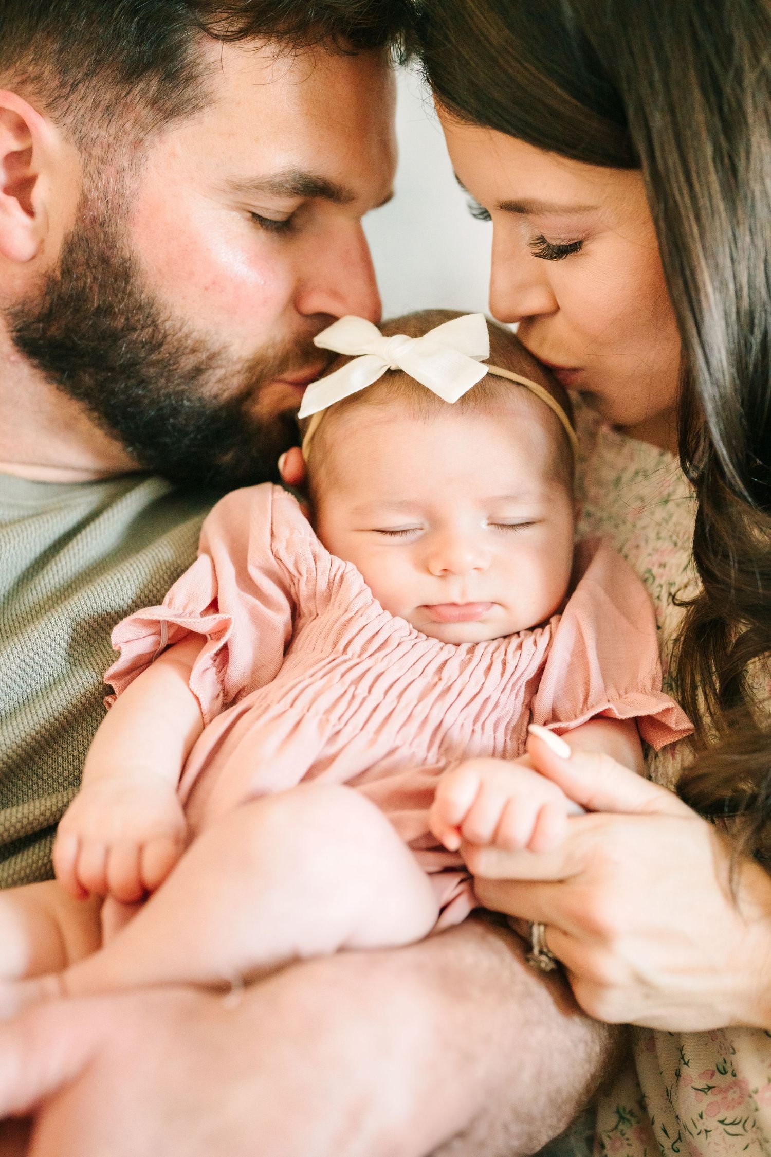 Intimate family moment with sleeping baby in pink dress surrounded by love.
