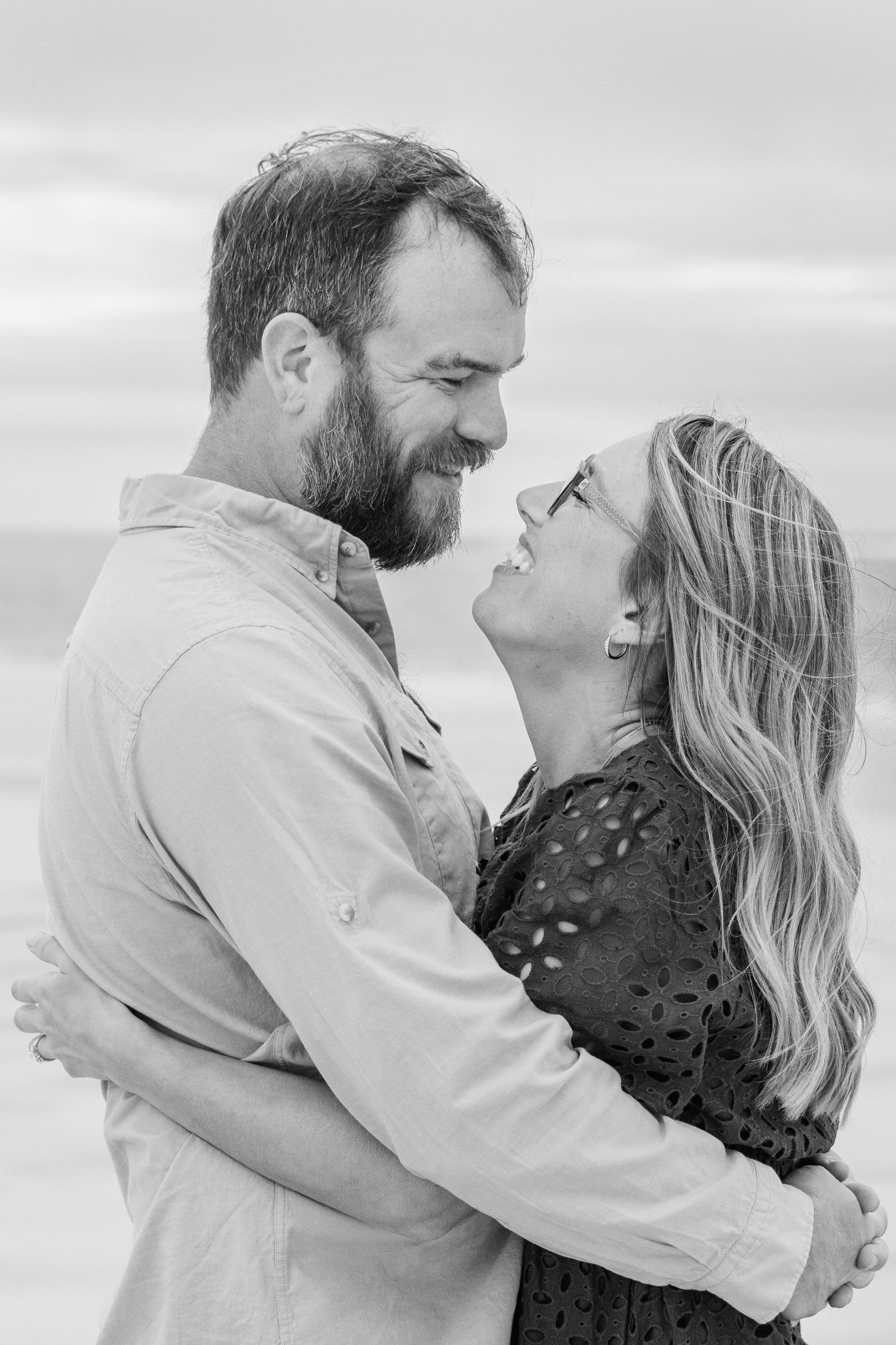 A joyful couple shares an intimate moment against an overcast sky in black and white.