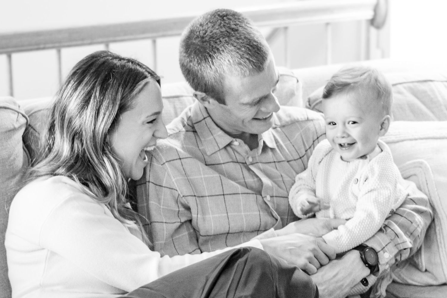 A family shares a joyful moment together while sitting on a bed in a bright room.