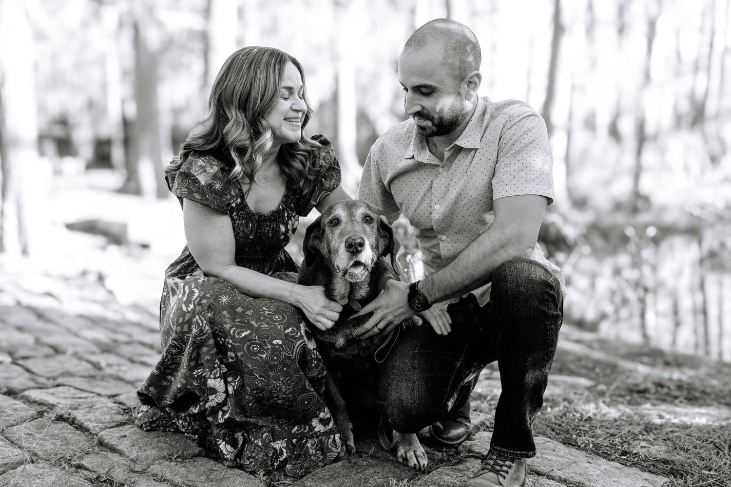 Black and white portrait of couple with their dog on stone steps.