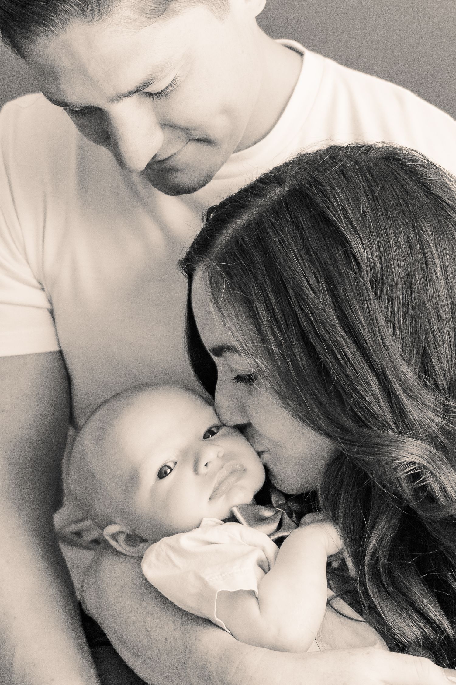 Intimate black and white portrait of parents sharing a tender moment with their newborn.