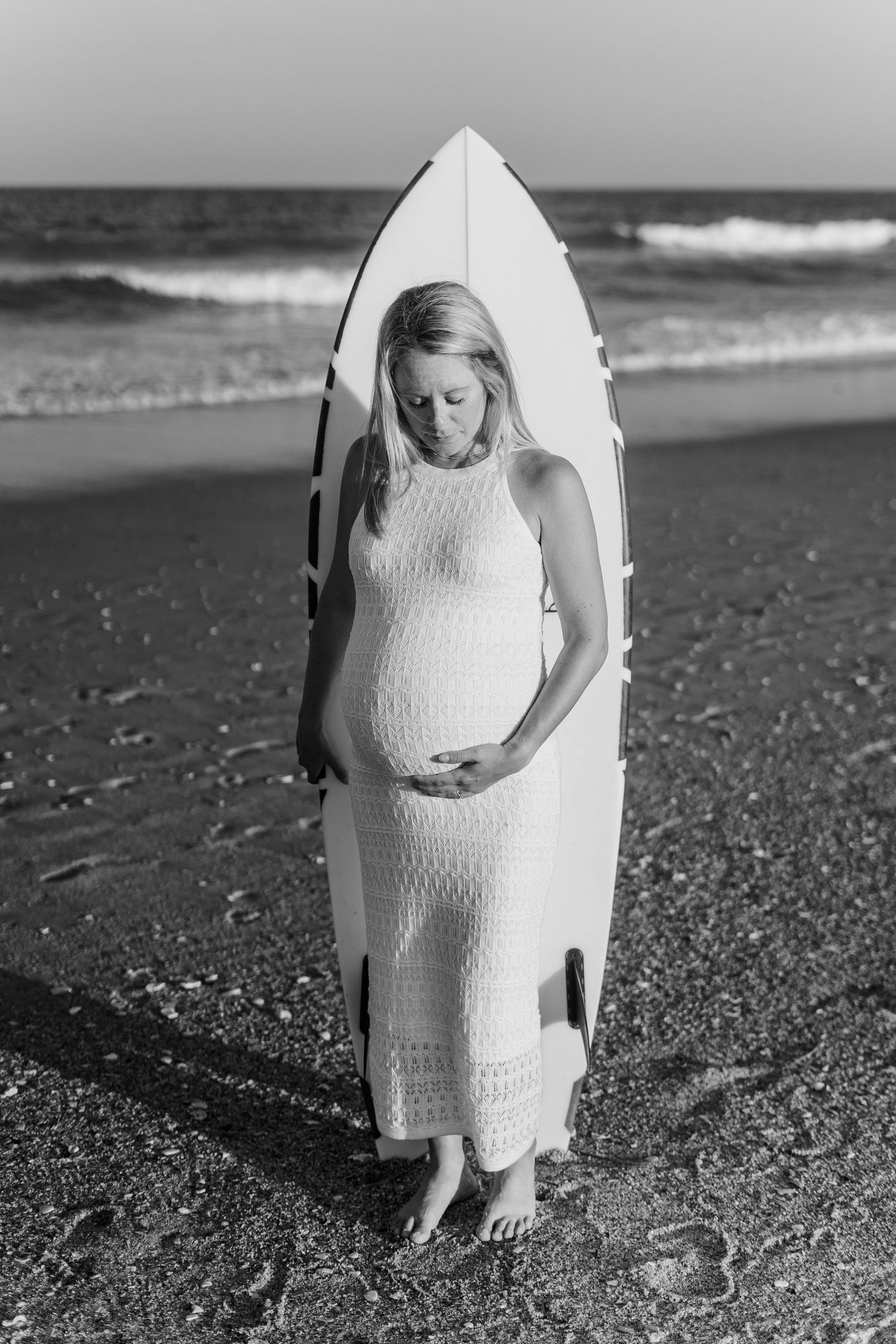 Black and white beachside maternity photo with a surfboard as a creative backdrop.