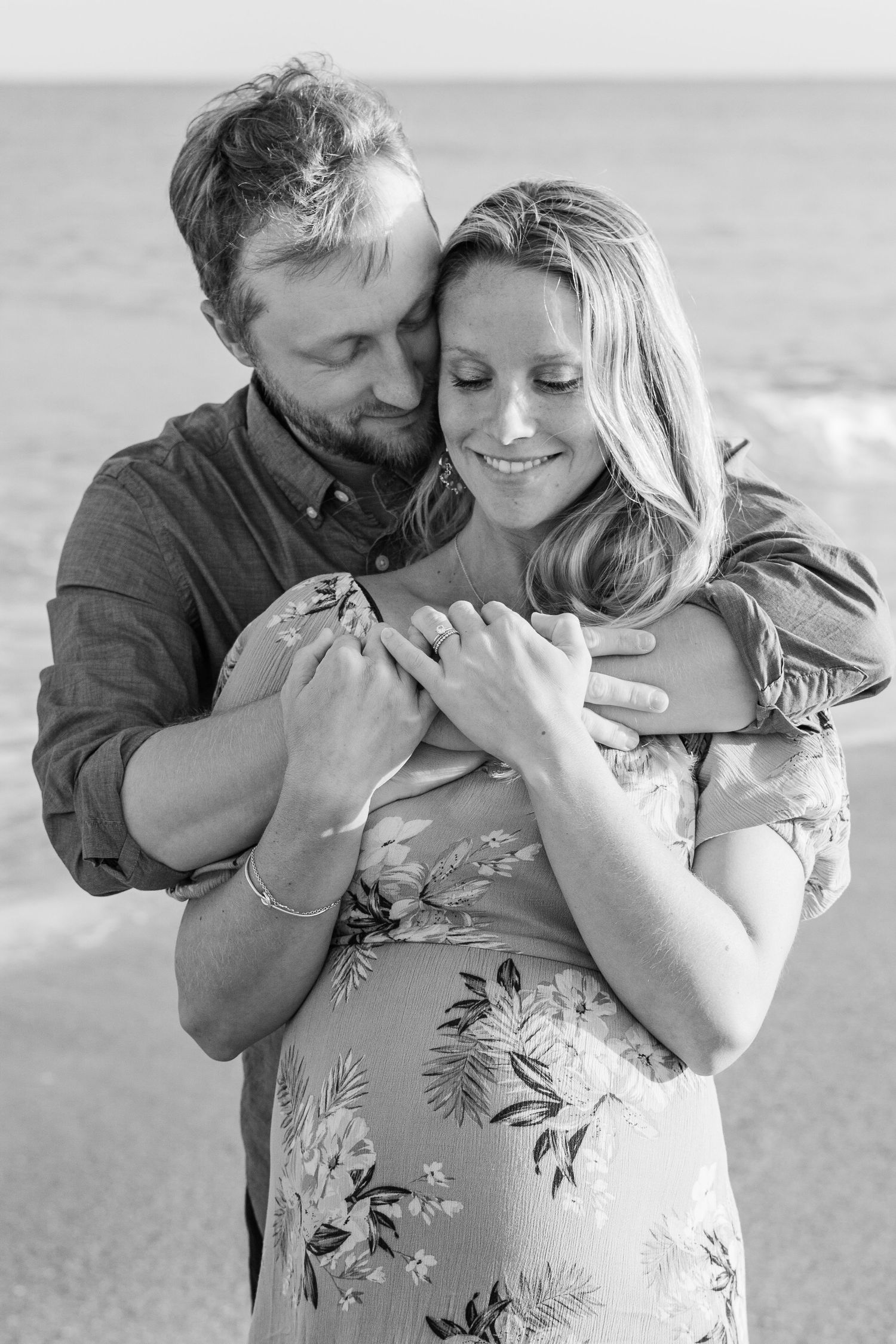 Black and white portrait of couple embracing on beach during maternity session.