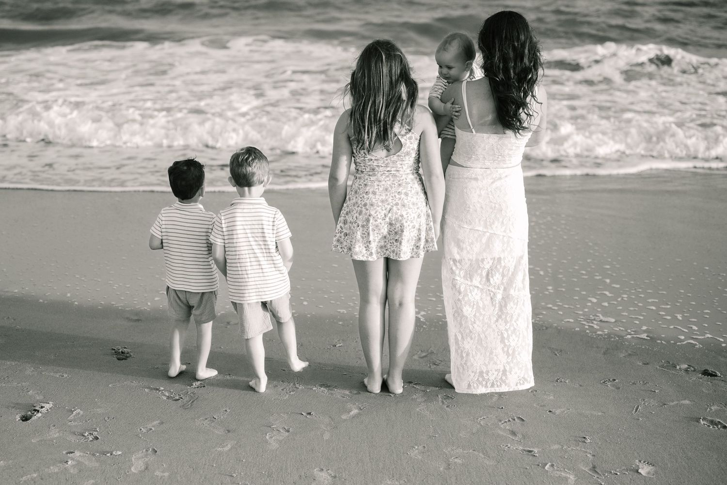 Back view of family standing together at ocean's edge in black and white.