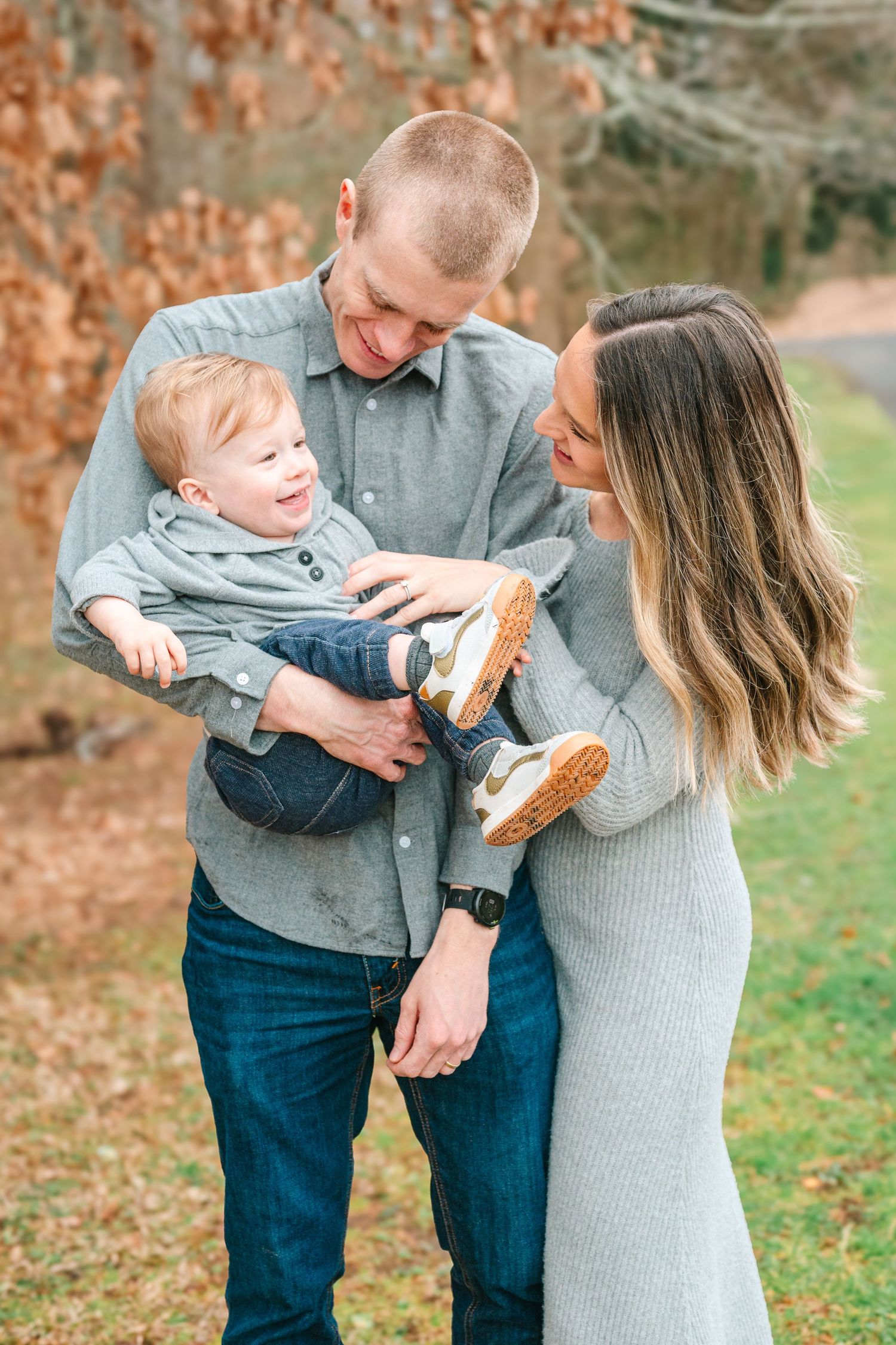 Happy family shares joyful moment outdoors in autumn with laughing toddler wearing blue clothes and brown shoes.
