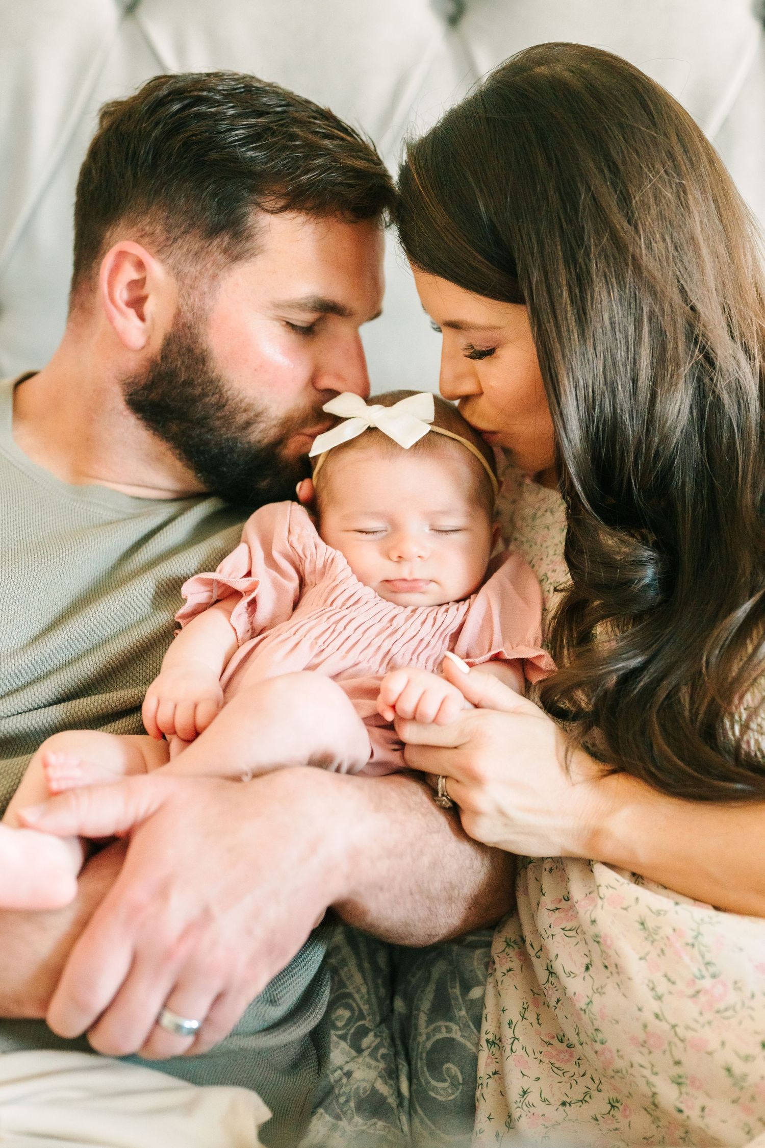 Sleeping baby in pink onesie rests peacefully between parents sharing an intimate family moment.