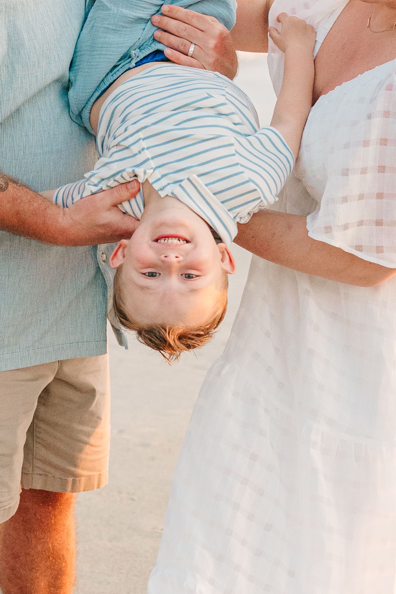 Playful upside down portrait of child in striped shirt during beach family photoshoot.