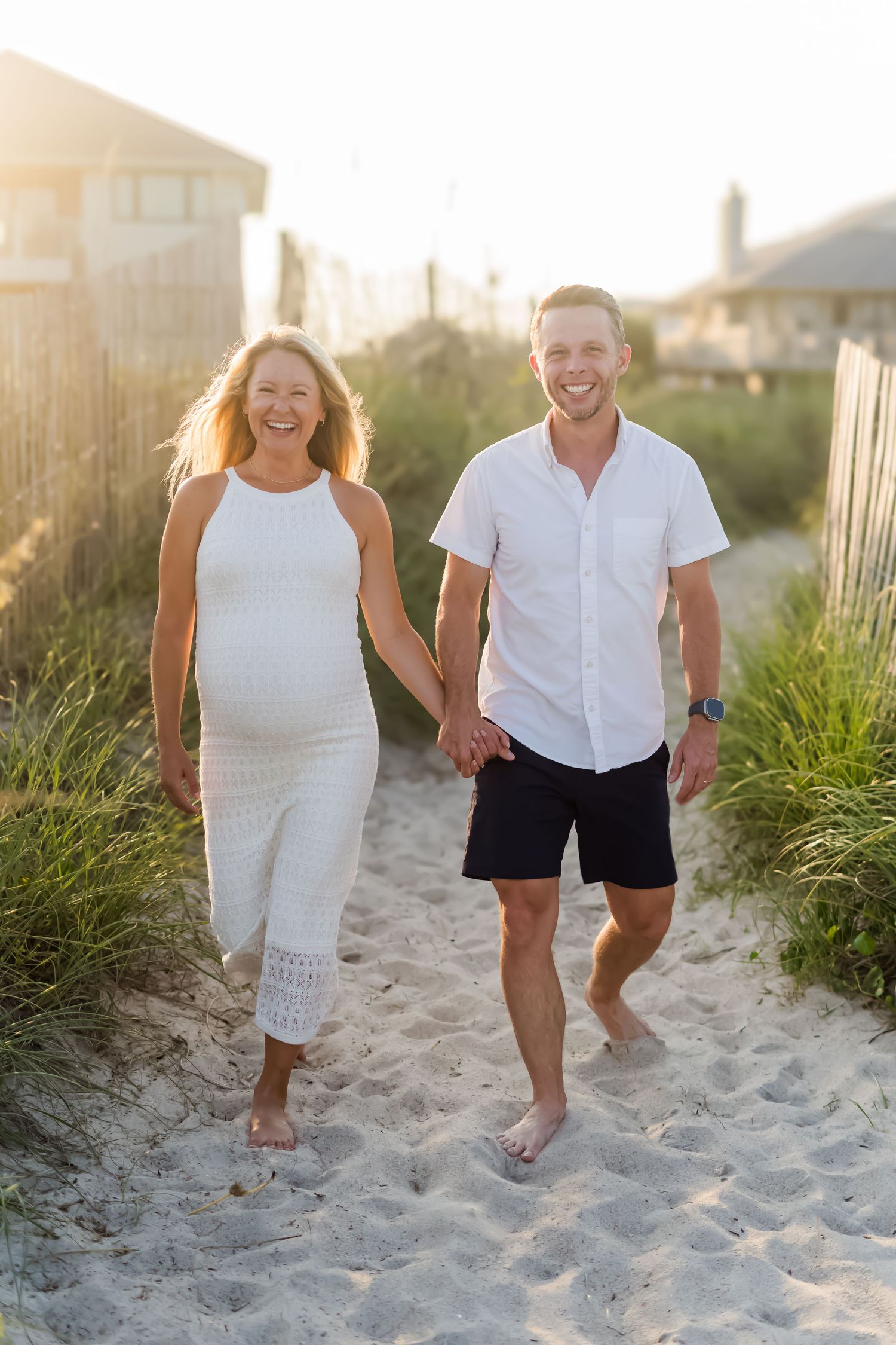 Happy couple walks hand in hand along sandy beach path during golden hour.
