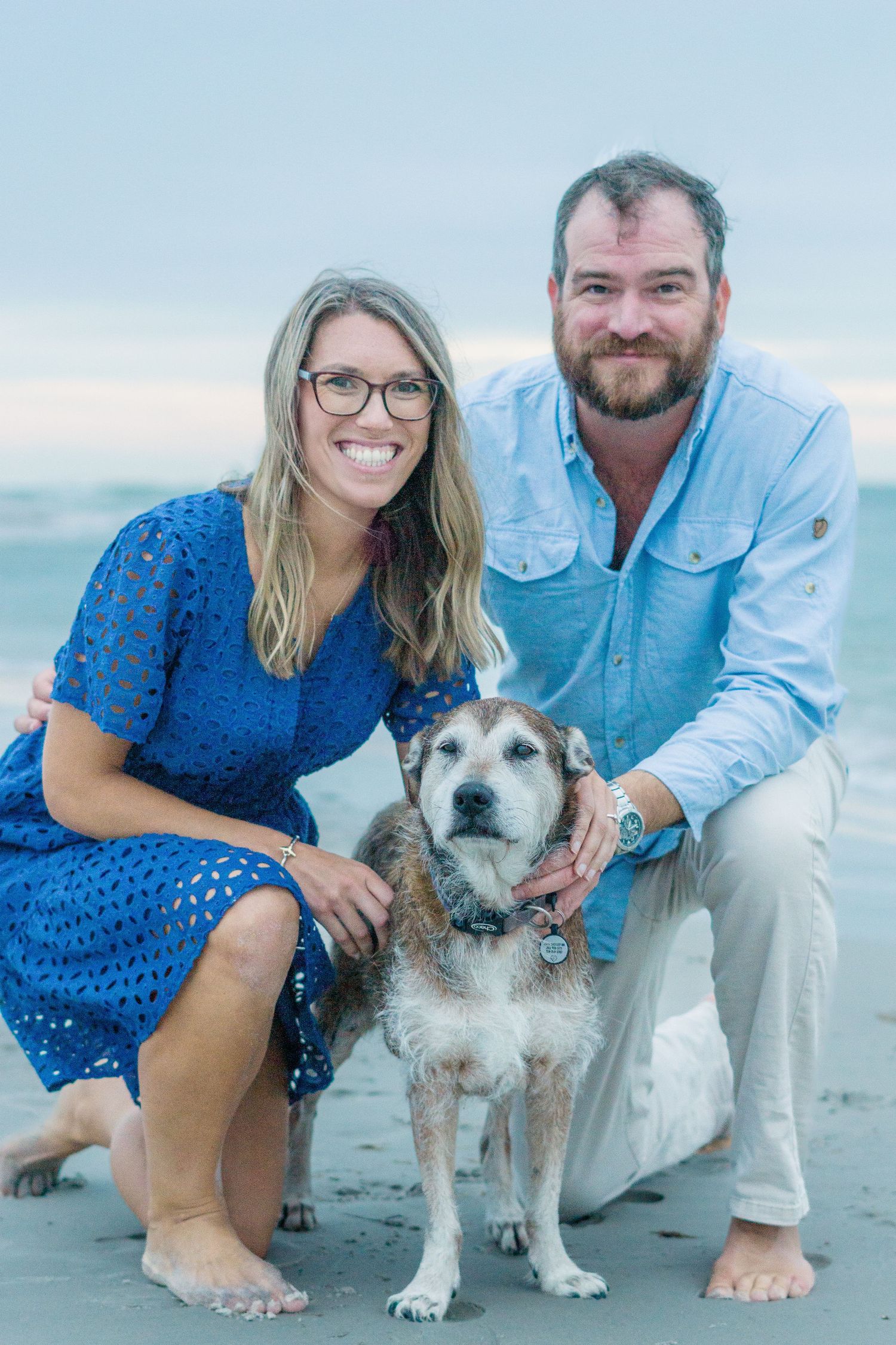 Happy couple poses with their senior dog on a beach during a family photoshoot.
