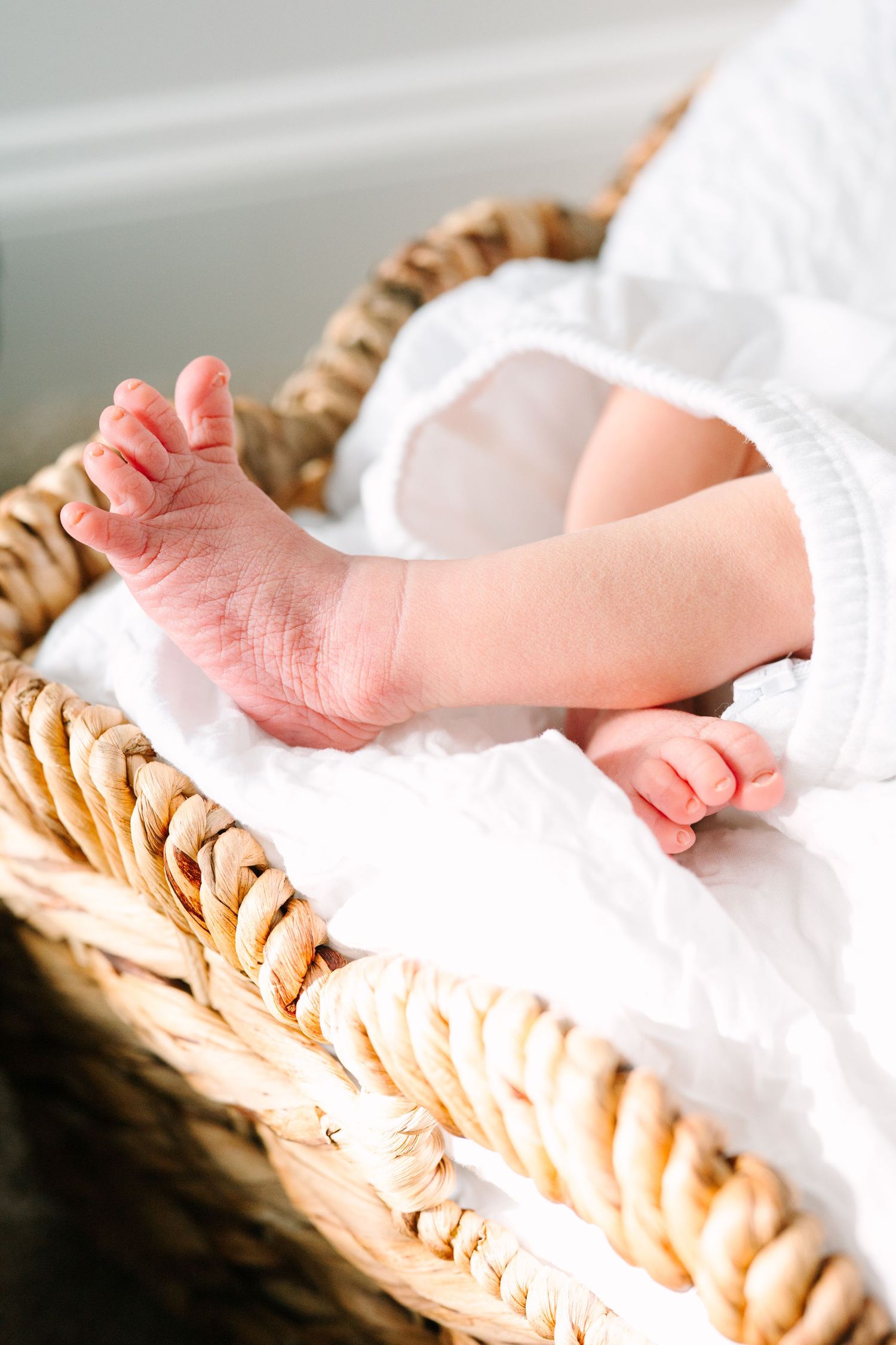 Tiny pink baby feet resting on soft white fabric in a woven basket.