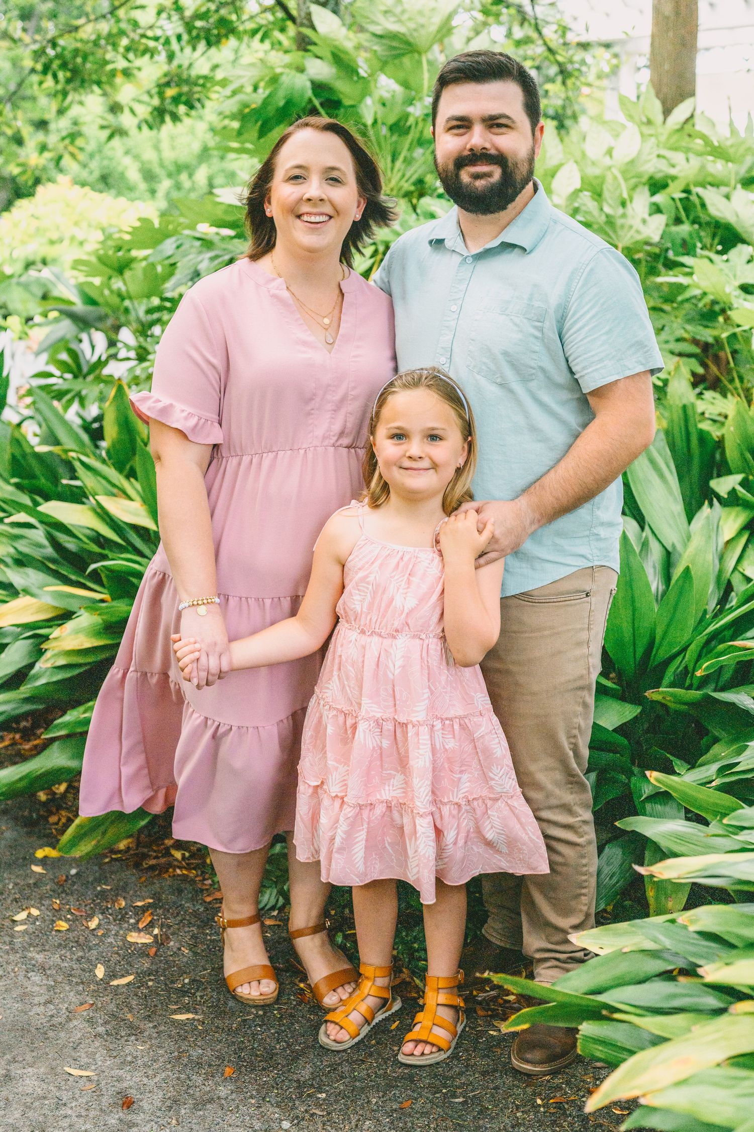 A family poses together in coordinating pink outfits against a lush green garden backdrop.