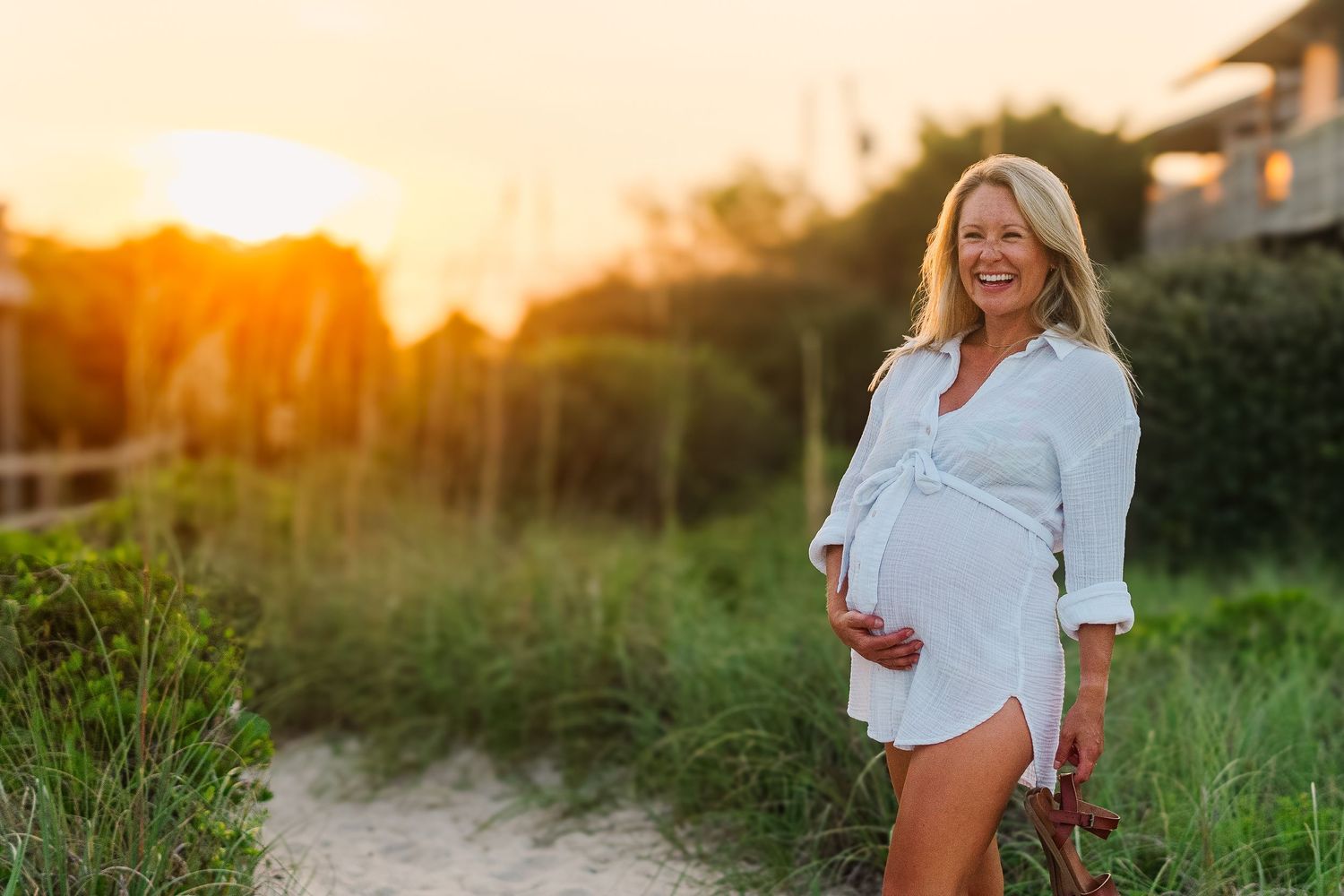 Maternity photo shoot at sunset showing expectant mother in white shirt on sandy beach.