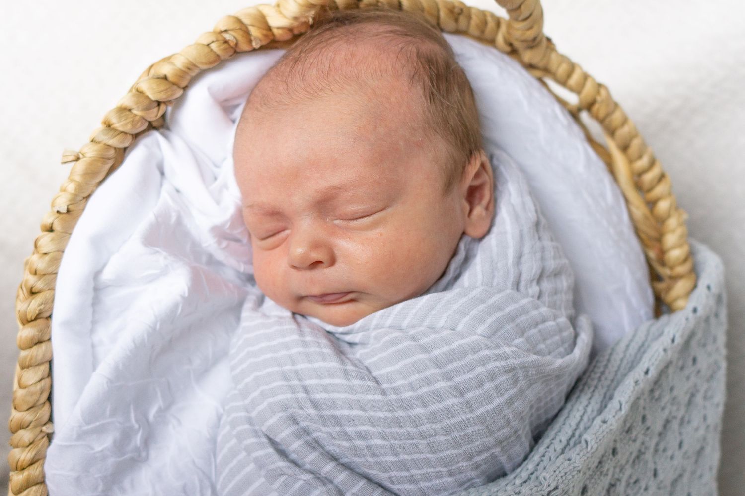 Sleeping newborn wrapped in soft gray blanket resting peacefully in woven basket.