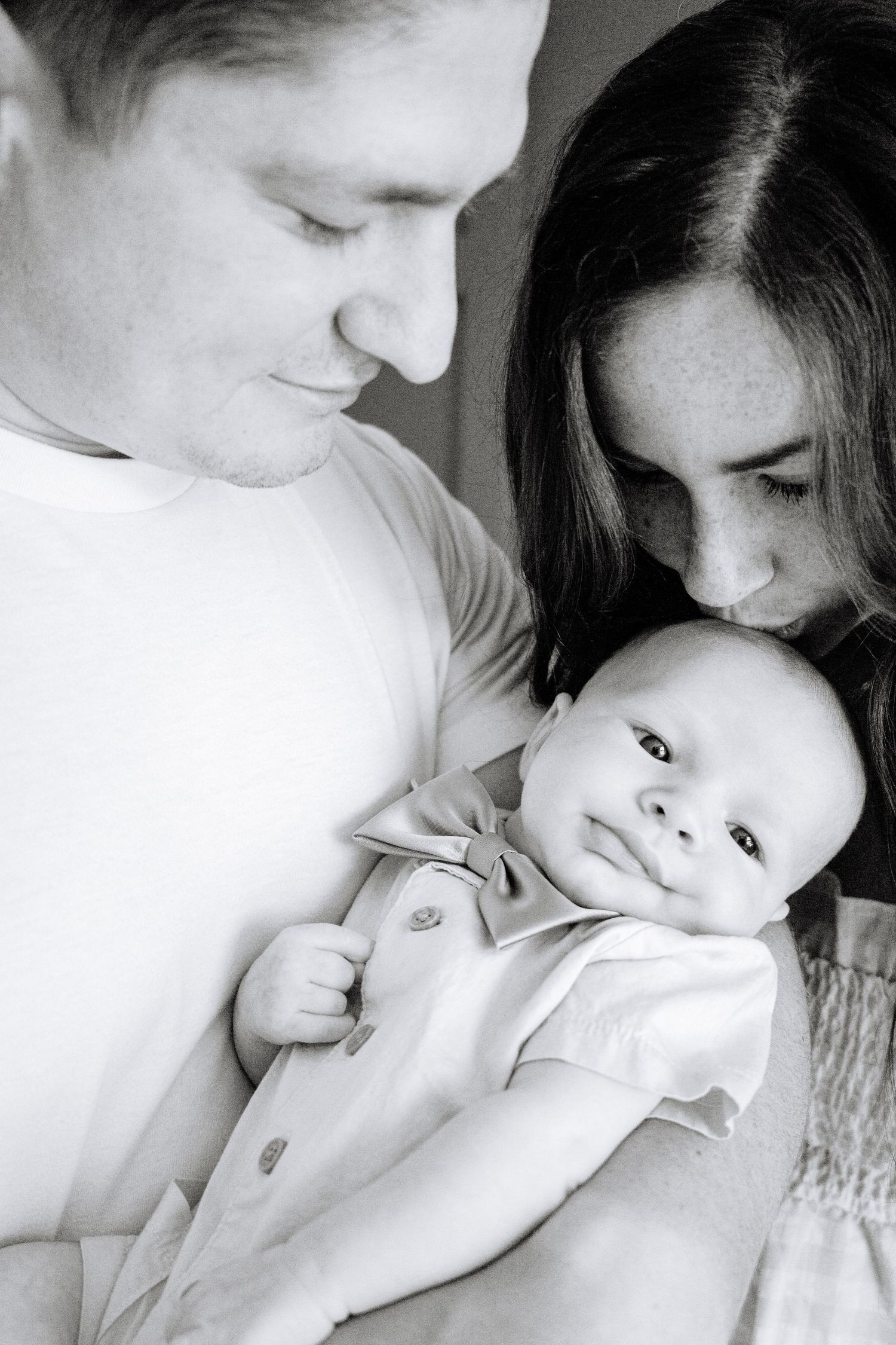 Black and white portrait of infant with parents in tender moment.