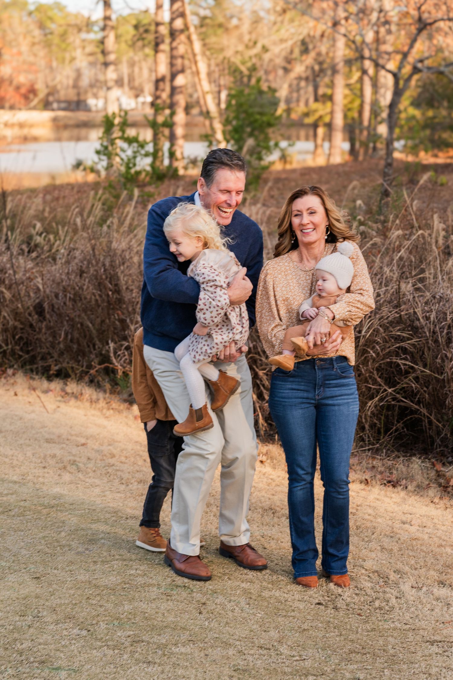 Happy family of four laughing together on a nature path with lake in background.