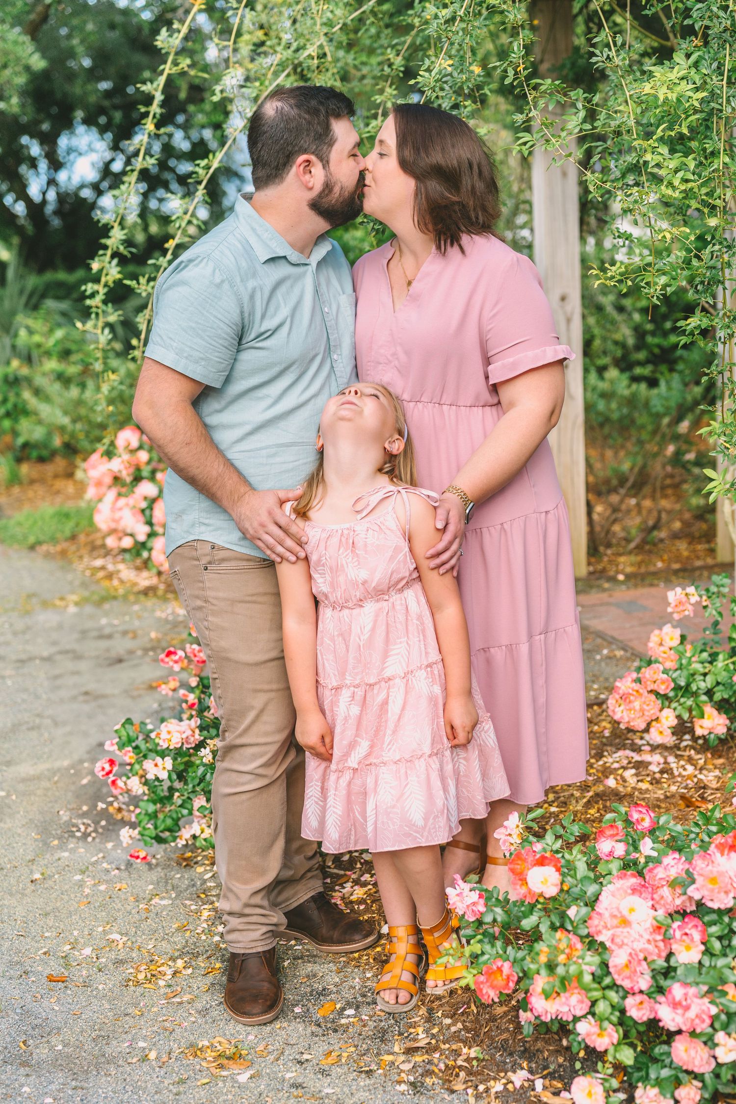 A family in coordinating pink outfits poses together among blooming flowers in a garden path.