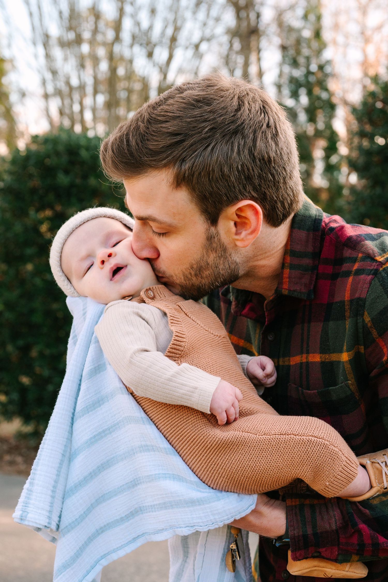 Tender moment between parent and baby wrapped in light blue blanket outdoors.