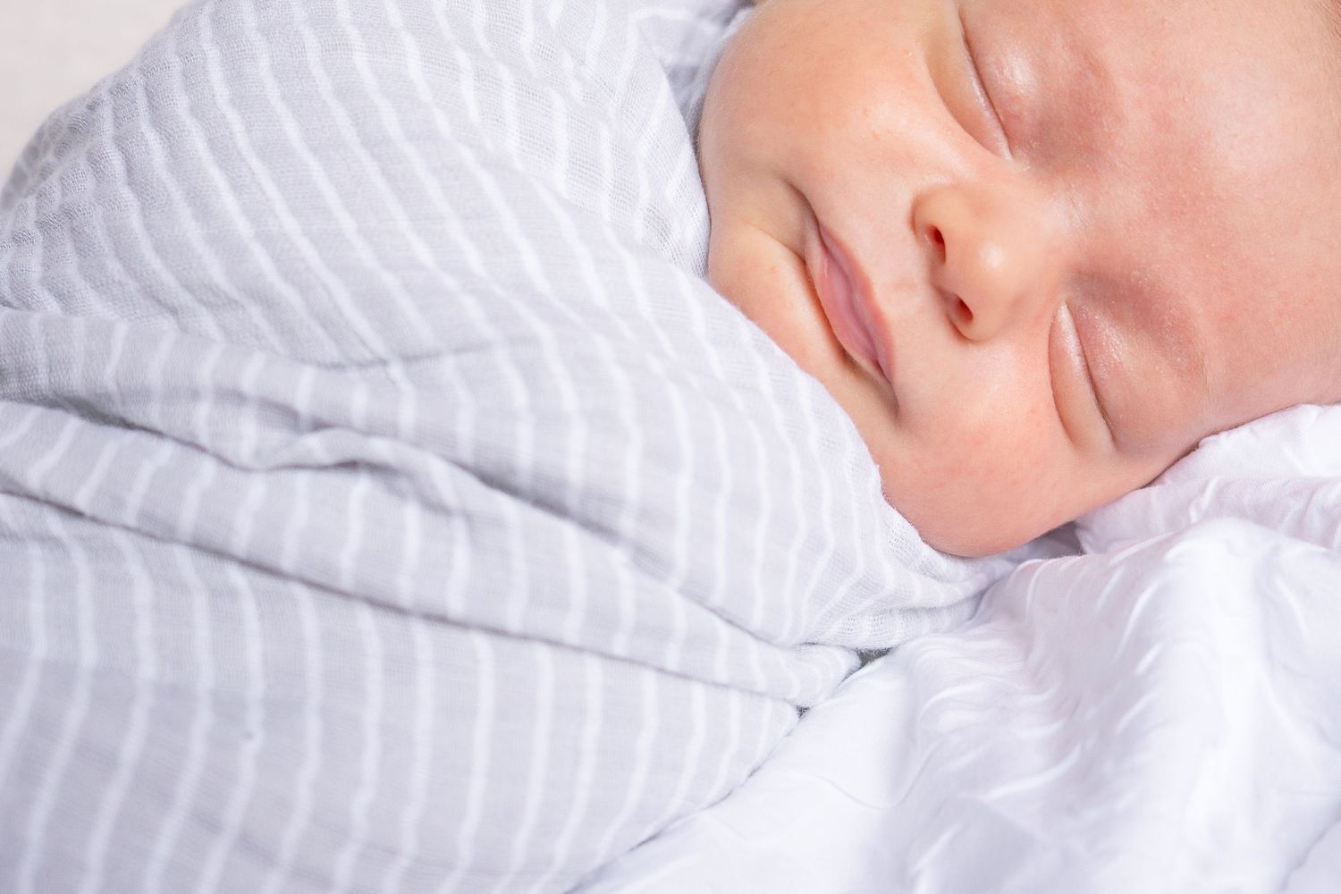 Close-up of sleeping baby wrapped in white striped bedding.