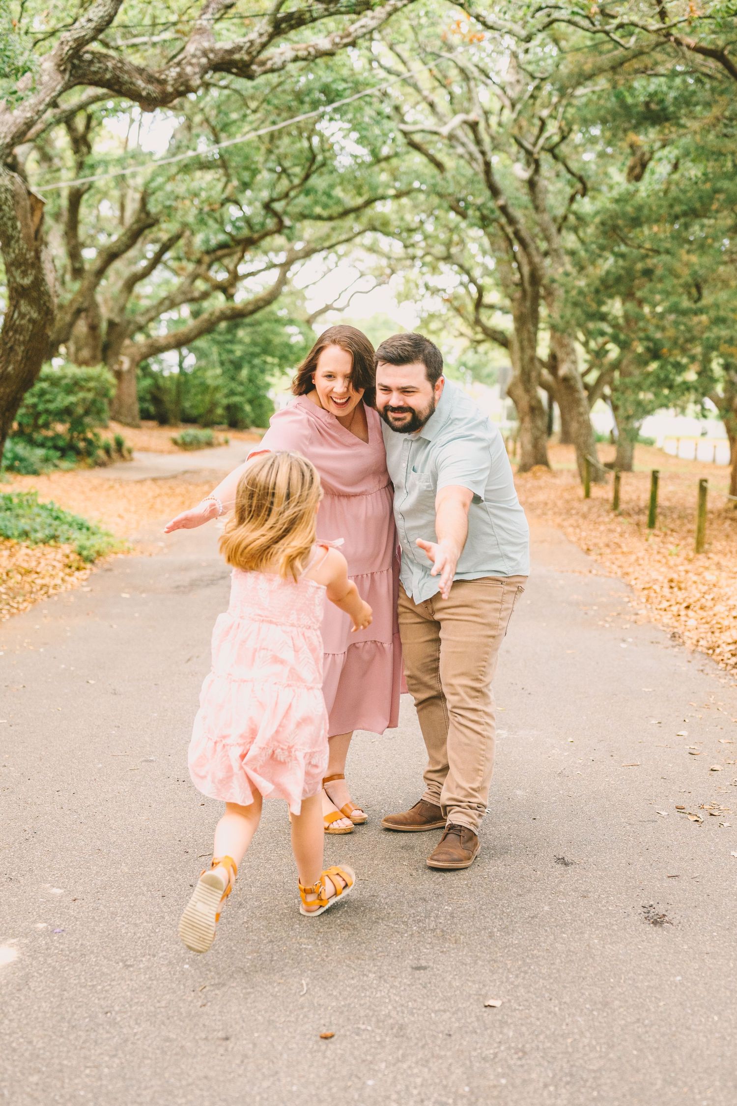 Family shares a joyful moment on a tree-lined path with autumn leaves scattered on the ground.