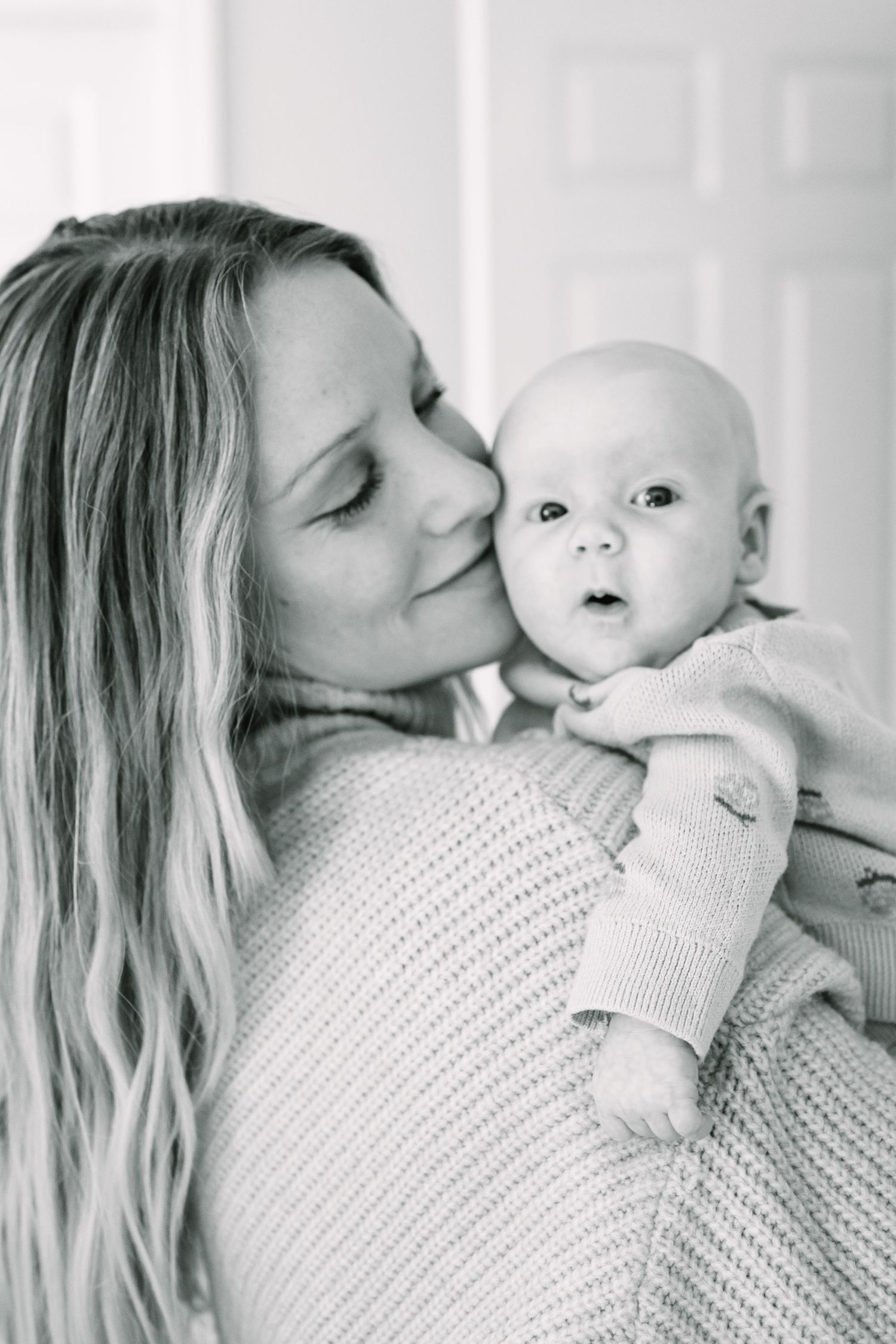 A tender black and white portrait of a mother cradling her young baby while gazing lovingly with closed eyes.