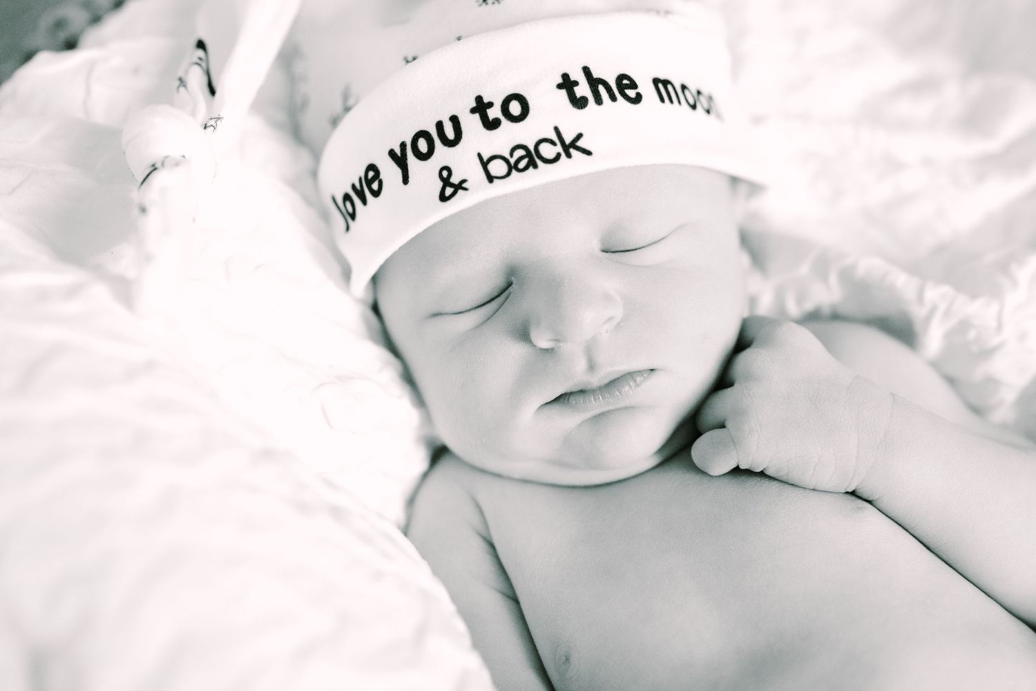 Black and white image of sleeping newborn wearing hat with text.